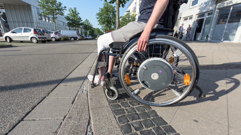 Ein Rollstuhlfahrer stoppt vor einer zu hohen Bordsteinkante.