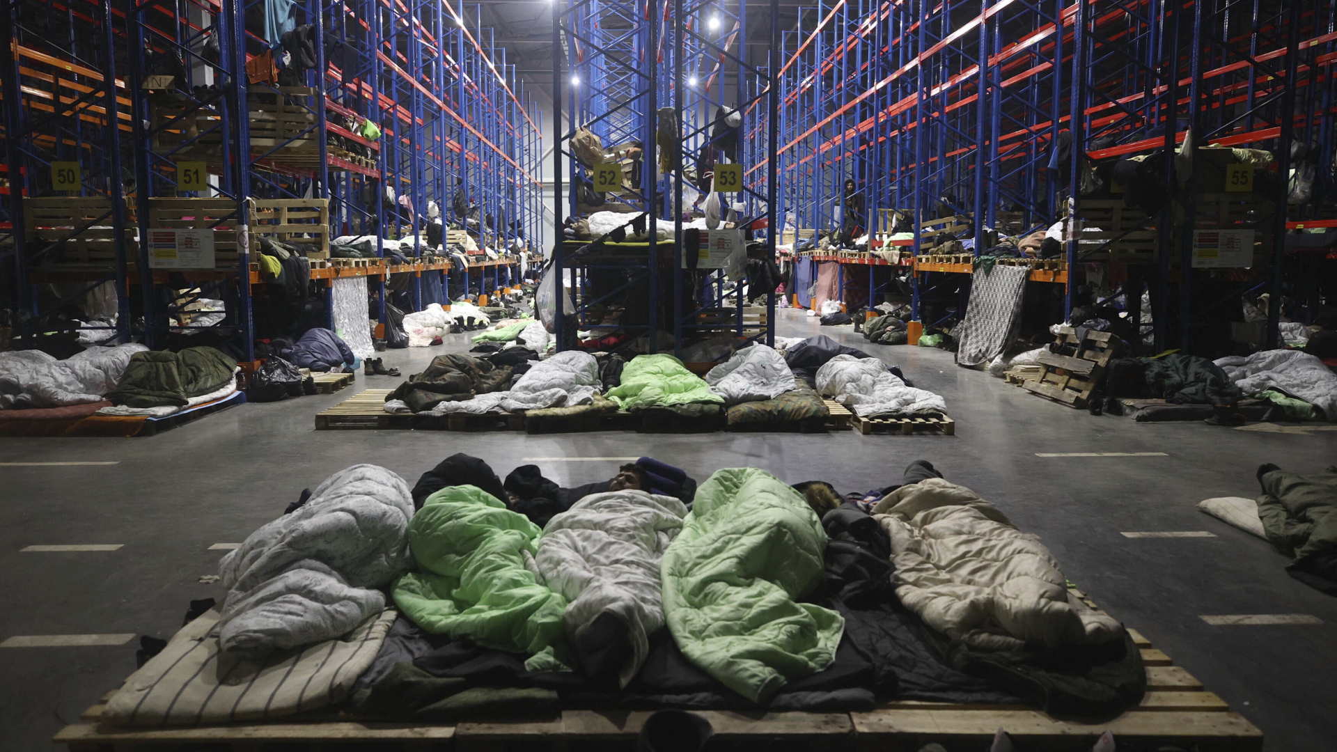 Migranten, die in Schlafsäcken auf Paletten in einem Logistikzentrum am Kontrollpunkt Kuznitsa in der Nähe der polnisch-belarusischen Grenze liegen. | dpa