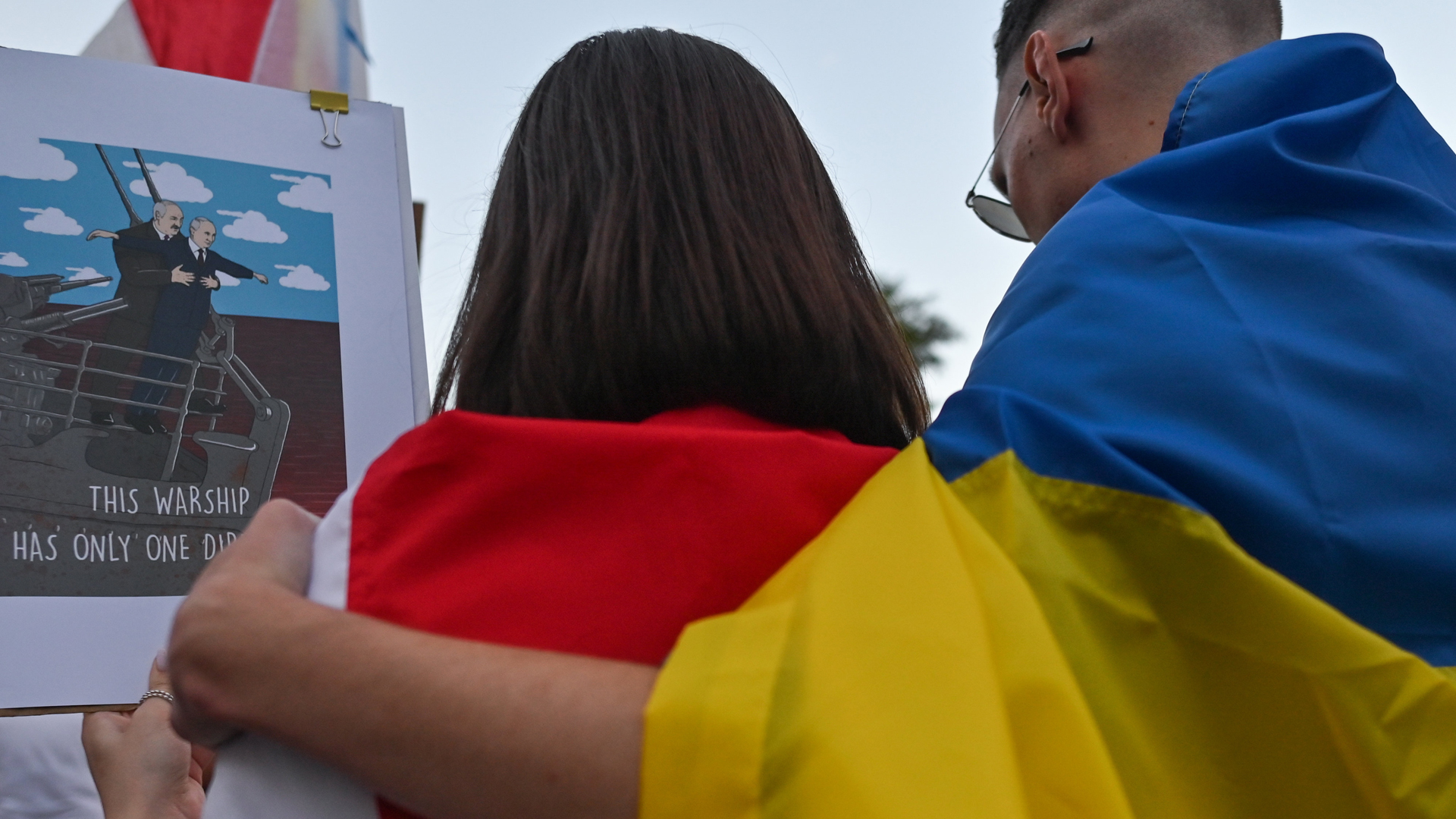 Ein Protestteilnehmer mit ukrainischer Flagge um die Schultern umarmt eine Protestteilnehmerin mit der weiß-rot-weißen Flagge der belarusischen Zivilgesellschaft. | picture alliance / NurPhoto