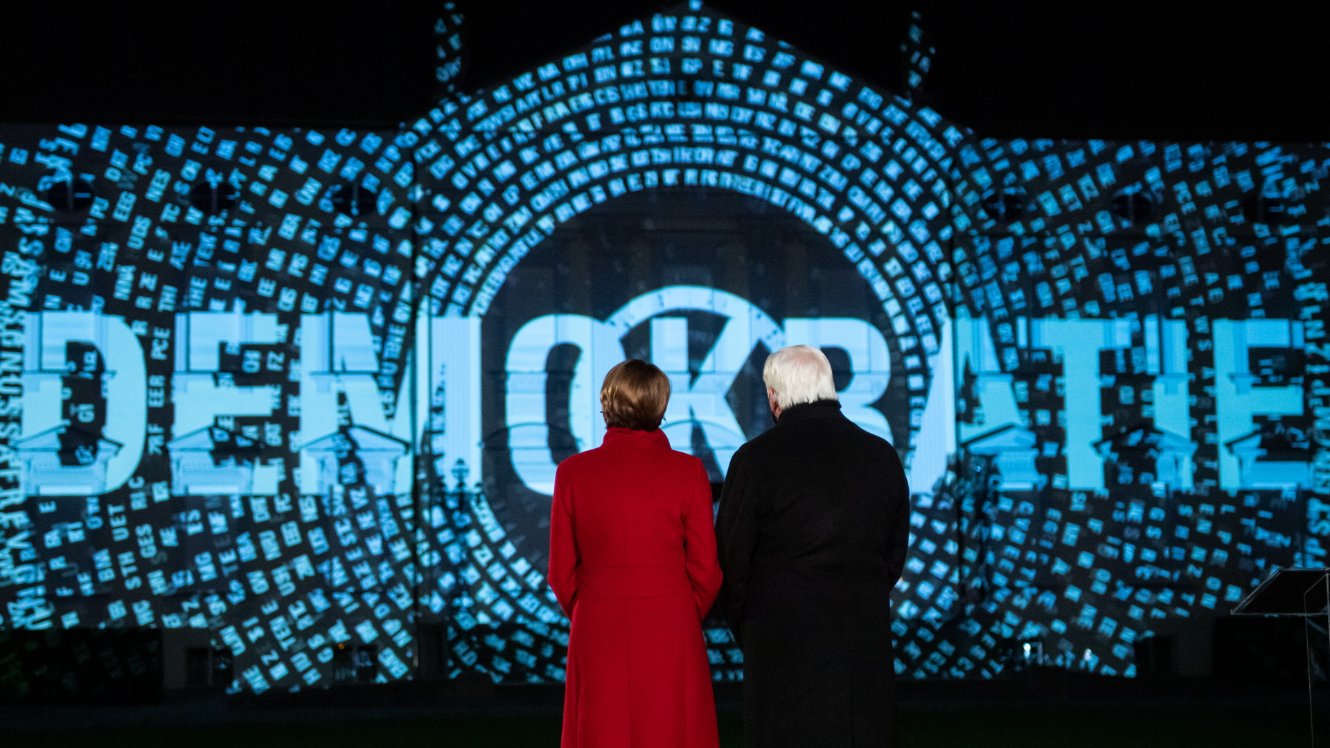 Bundespräsident Steinmeier und seine Frau blicken auf eine Lichtinstallation am Schloss Bellevue.