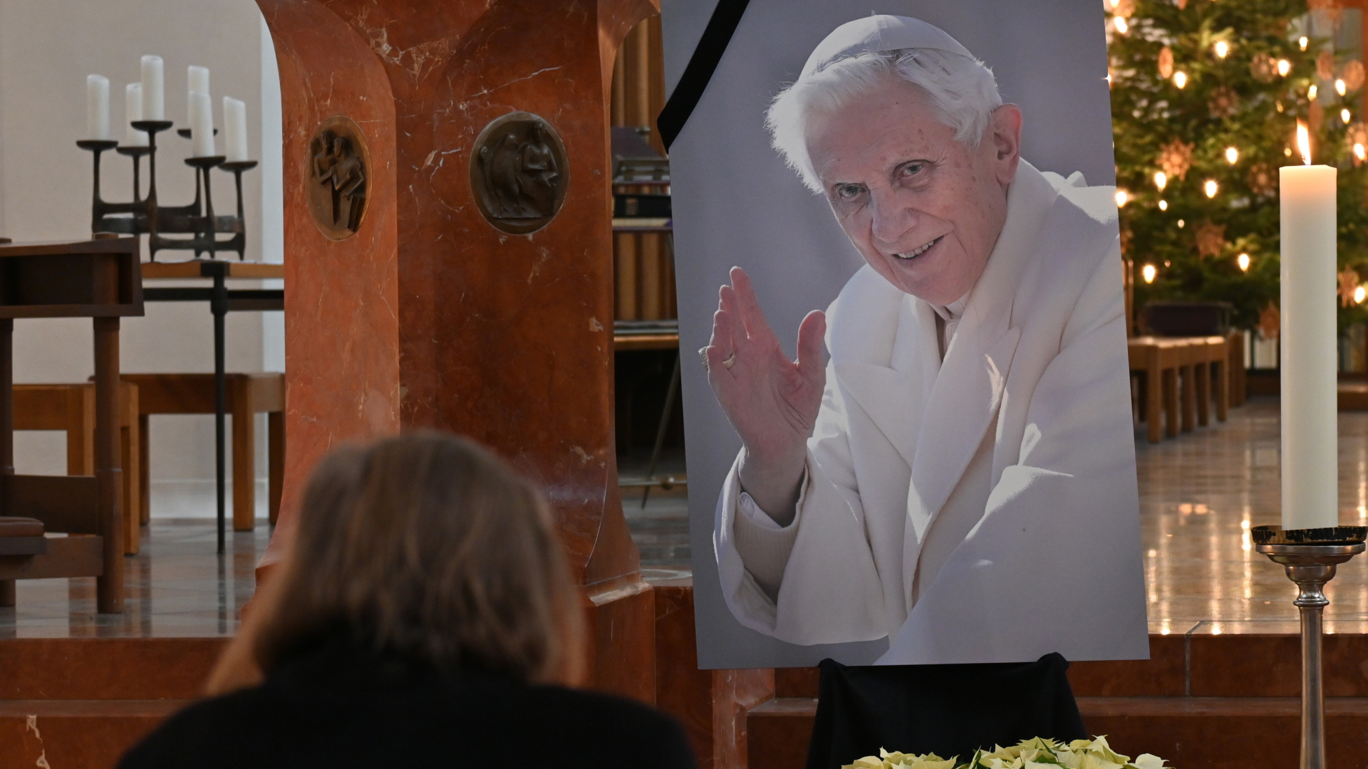 Eine Frau betet vor einem Bild des verstorbenen emeritierten Papst Benedikt XVI. in der Frauenkirche in München. | dpa