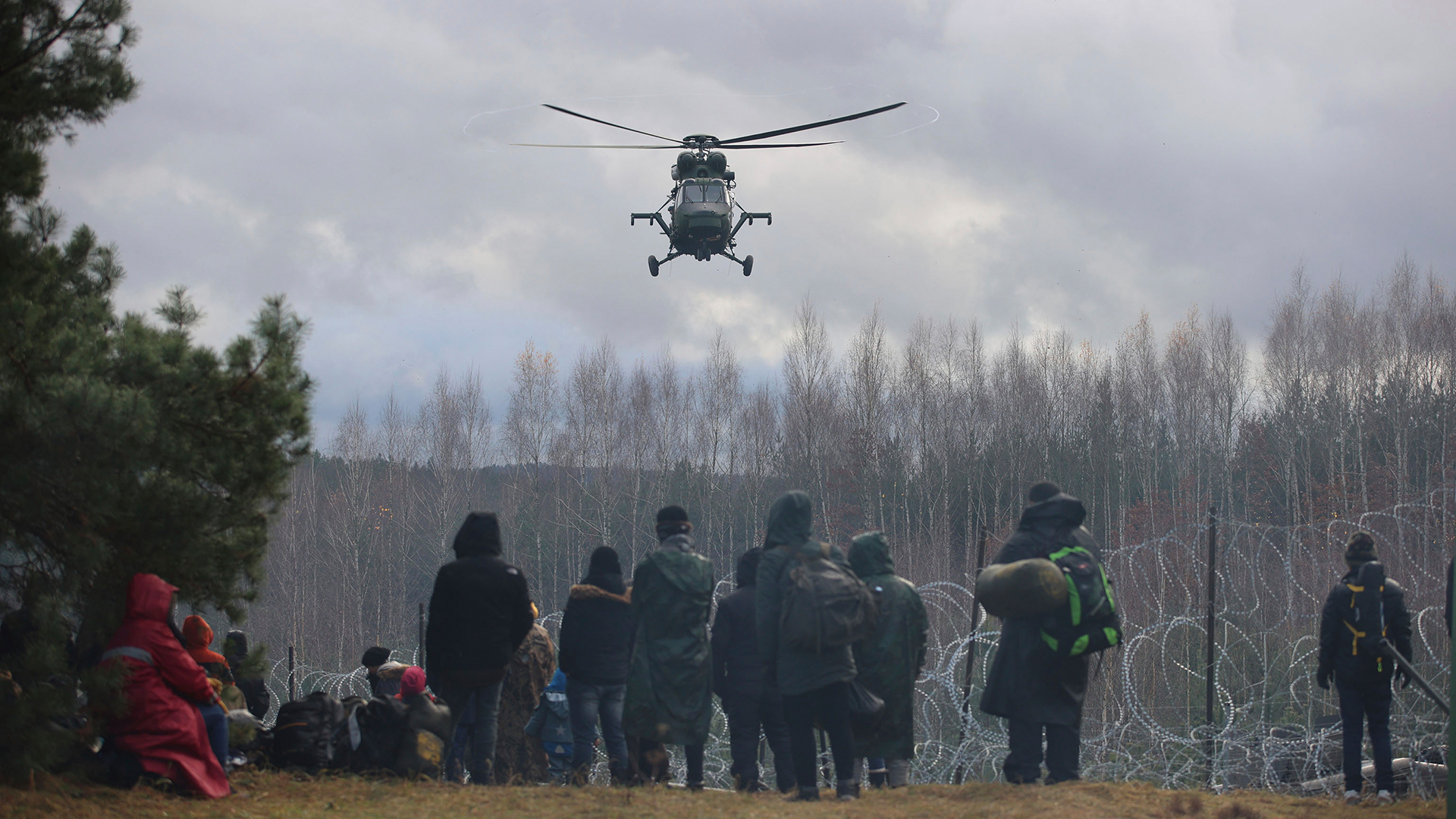 Ein polnischer Militärhubschrauber fliegt über eine Gruppe Migranten, die sich an der weißrussisch-polnischen Grenze versammelt haben. | picture alliance/dpa/BelTA/AP