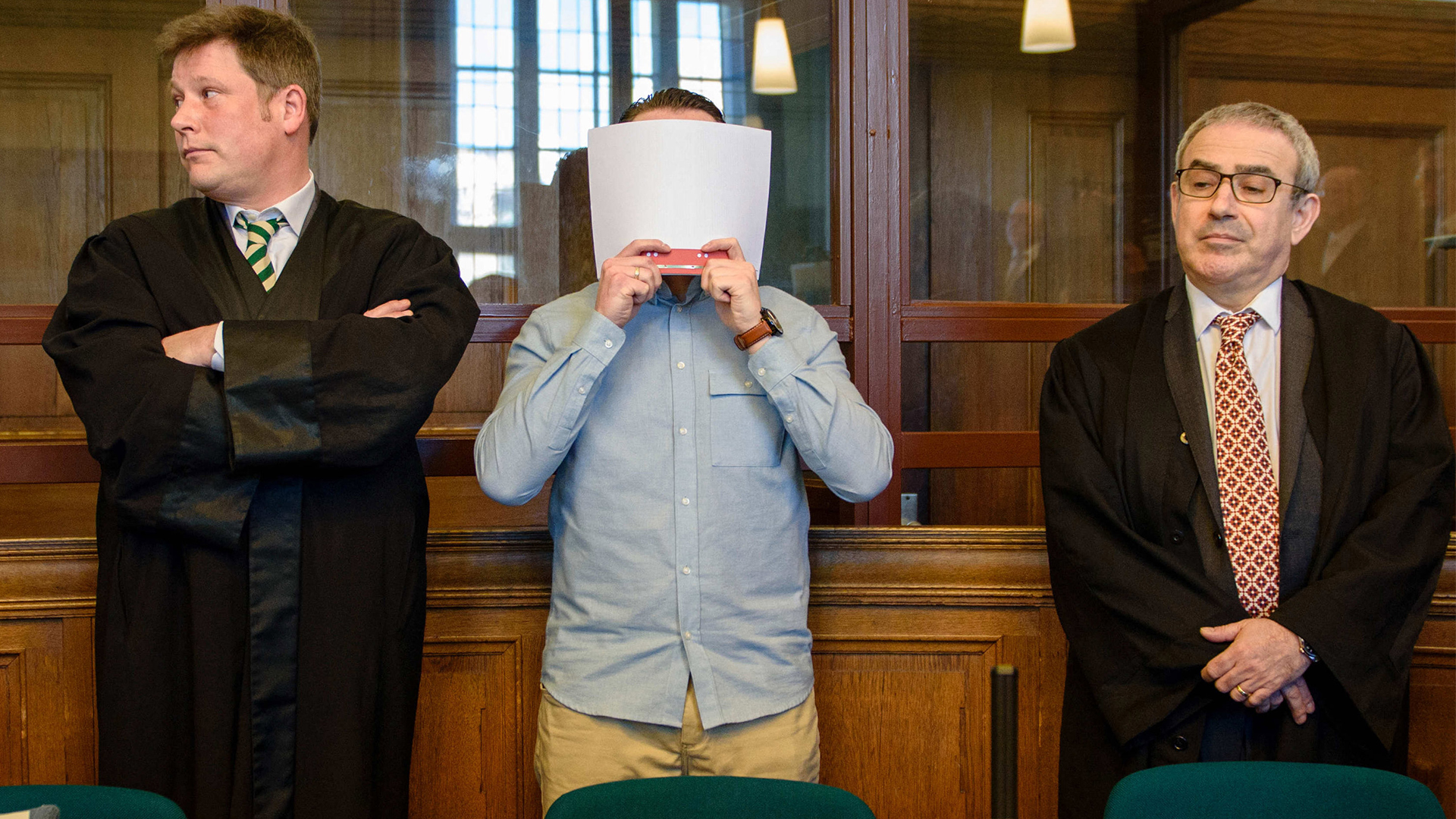 Der Angeklagte Hamdi H. steht in Berlin in einem Gerichtssaal des Landgerichtes Berlin zwischen seinen Anwälten und hält sich eine Akte vor das Gesicht. | dpa