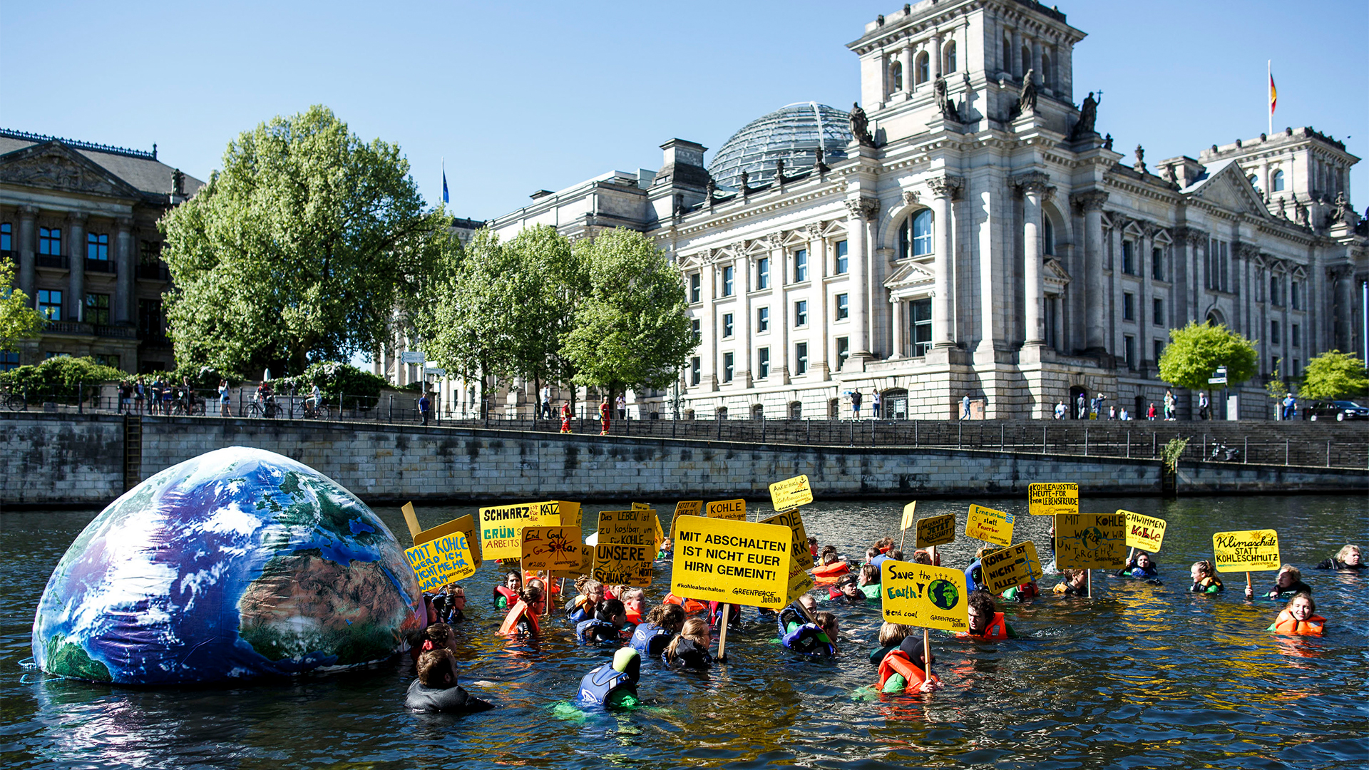 Aktivisten der Umweltschutzorganisation Greenpeace schwimmen am Reichstag in der Spree in Berlin. Mit der Aktion will die Organisation für mehr Klimaschutz demonstrieren. | dpa