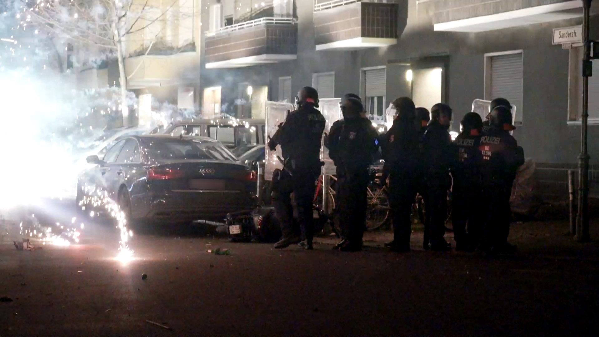 Polizeibeamte stehen neben explodierendem Feuerwerk. | dpa