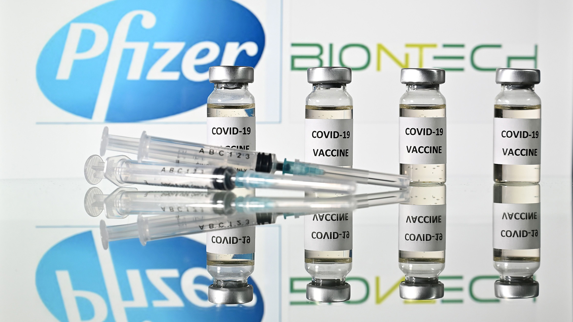 Ampullen und Spritzen liegen vor den Logos von Pfizer und BioNTech. | AFP