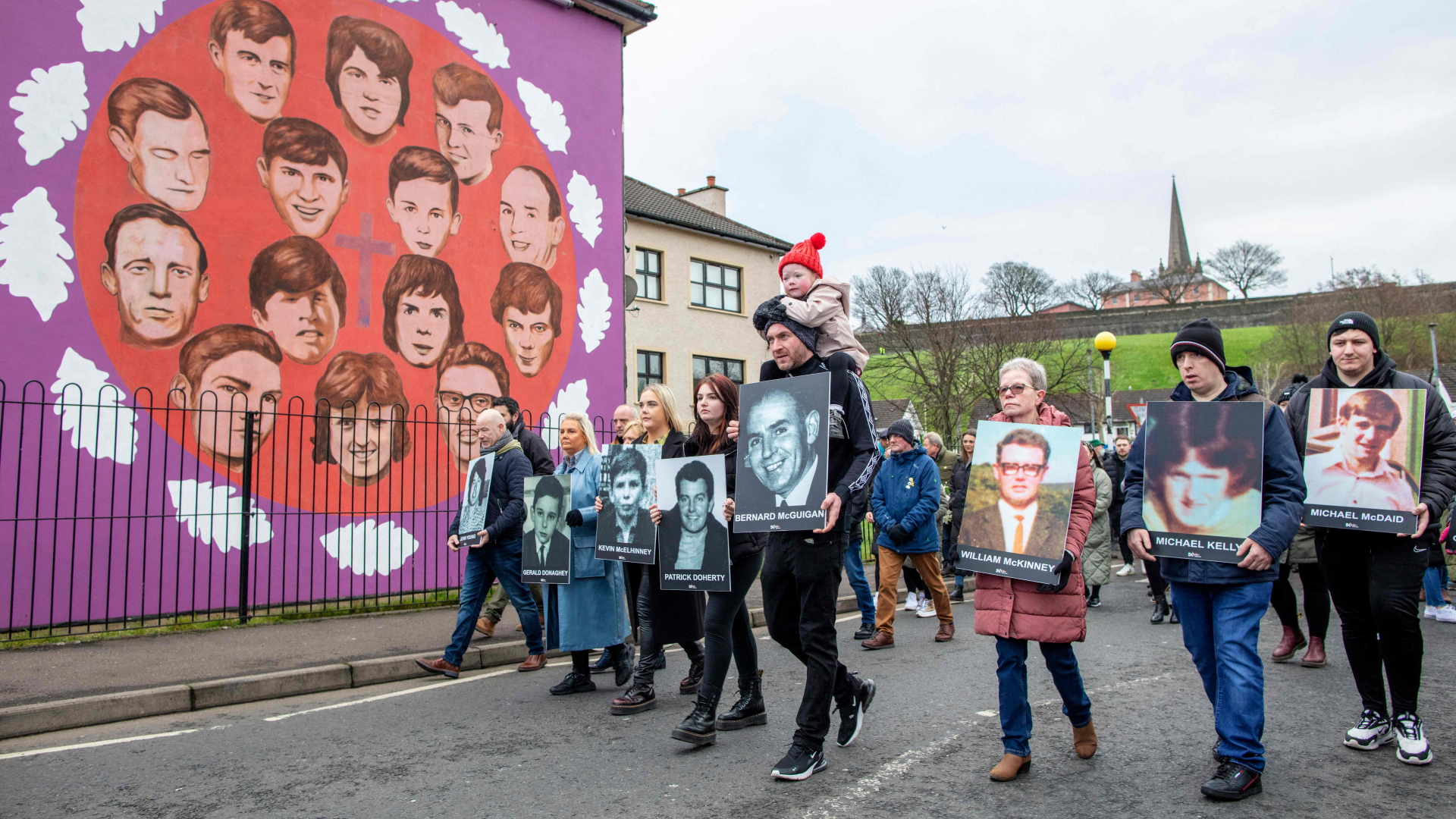 Teilnehmer des Gedenkmarschs gehen mit Fotos an einem Wandgemälde entlang, das die Opfer des Blutsonntags zeigt. | AFP