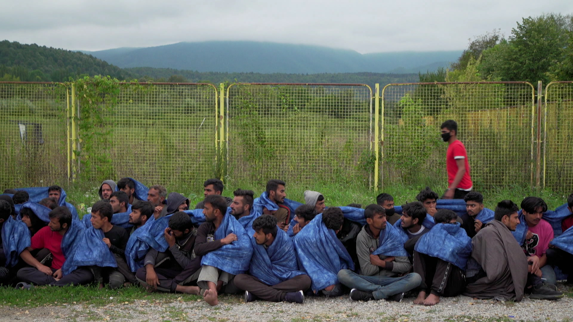 Männer in Wolldecken gehüllt sitzen vor einem Zaun | Simon Riesche