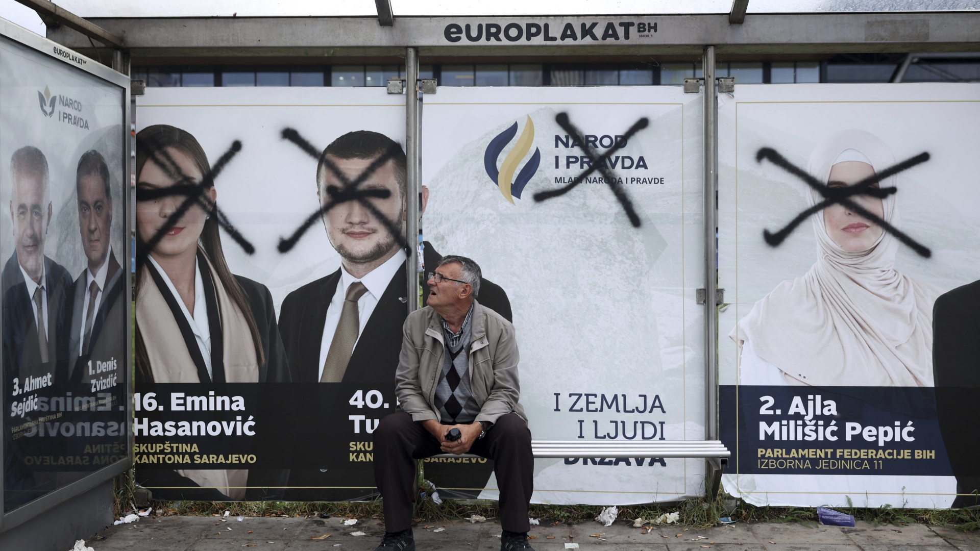 Ein Mann an einer Bushaltestelle in Sarajewo (Bosnien und Herzegowina) blickt auf beschmierte Wahlplakate