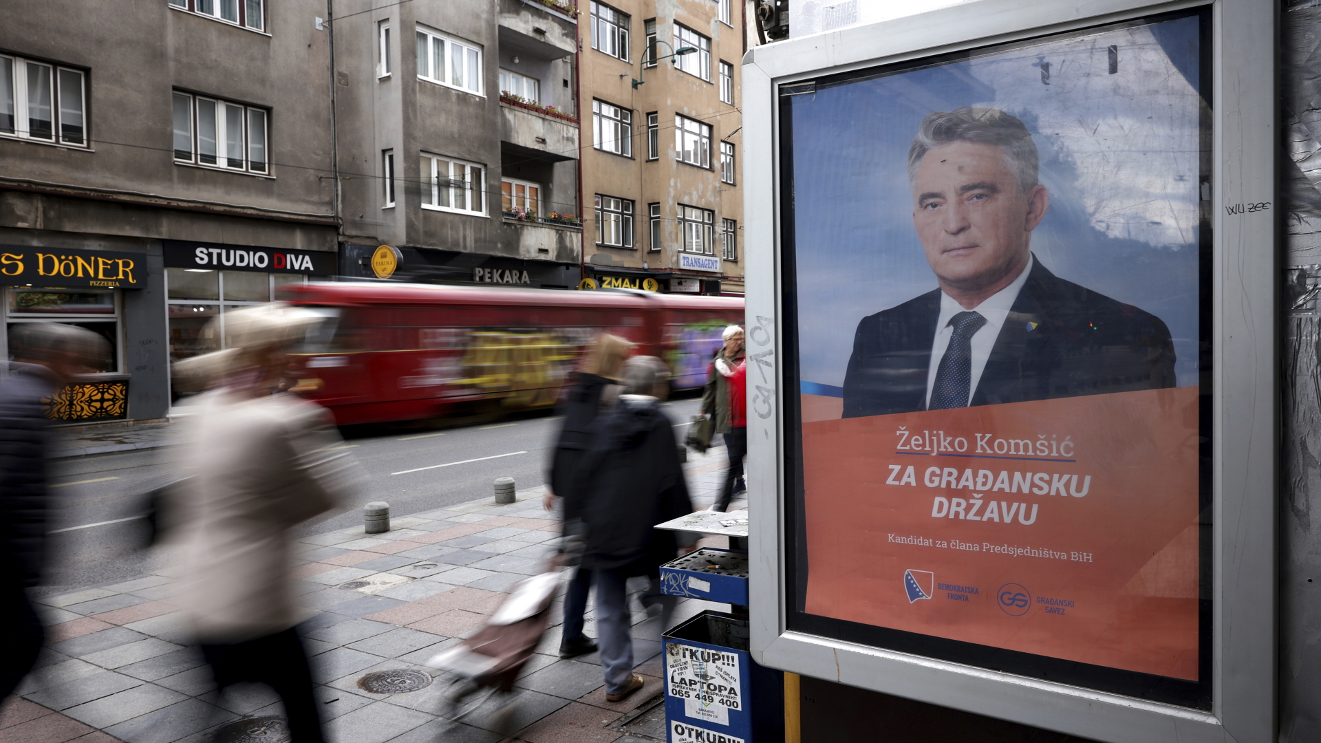 Menschen gehen an einem Wahlplakat von Zeljko Komsic vorbei, der bei den bevorstehenden Wahlen für das Amt des bosnischen Präsidenten kandidiert. | dpa