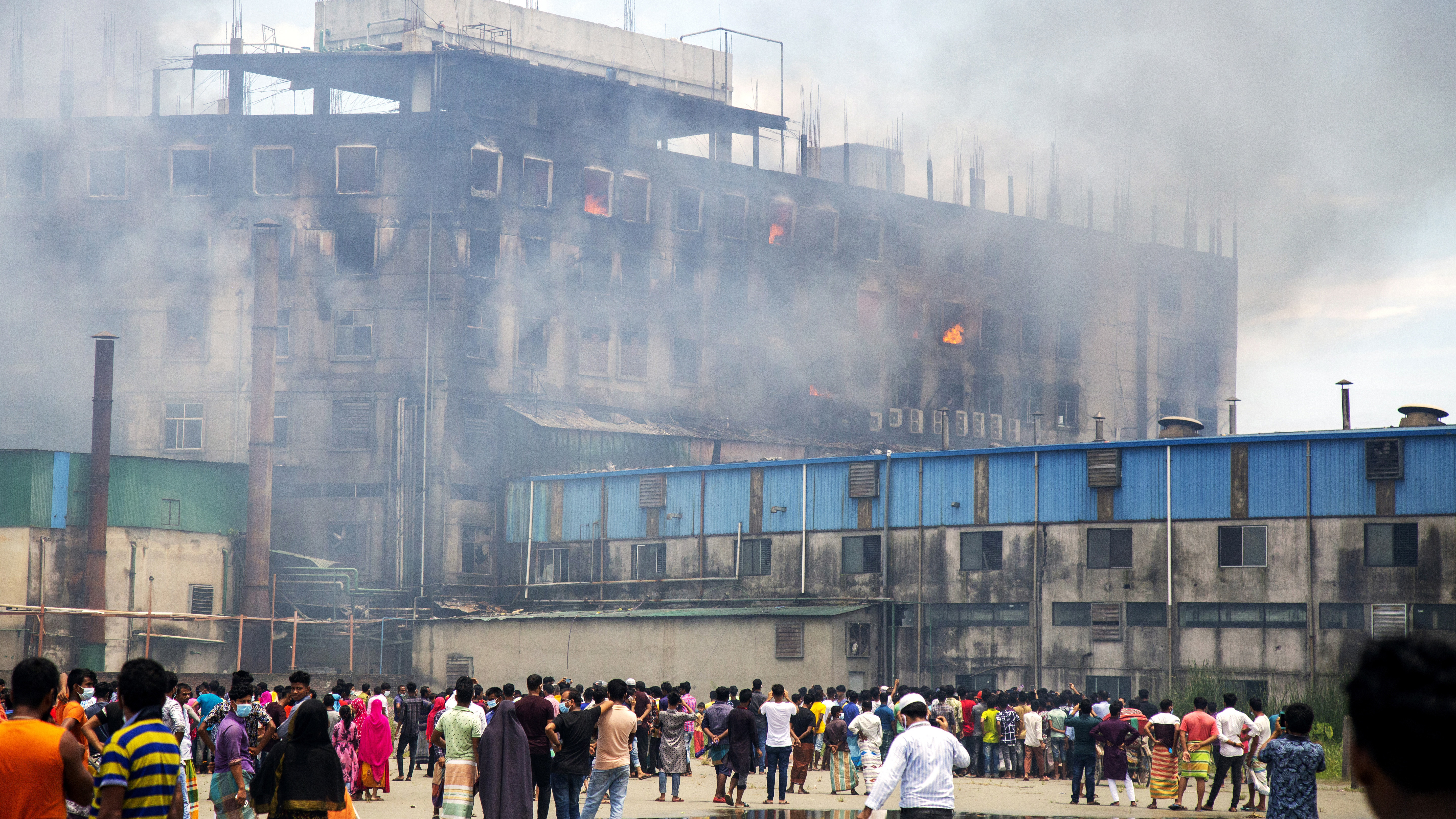 Arbeiter stehen vor einer brennenden Fabrik in Bangladesh. | EPA