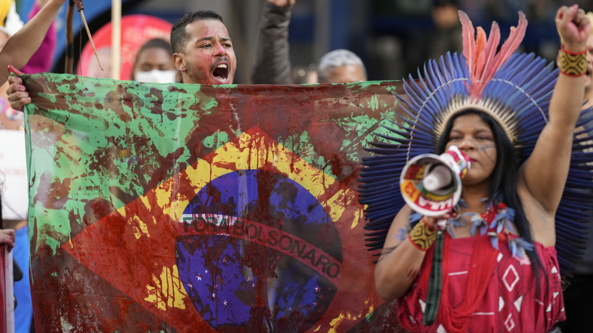 "Weg mit Bolsonaro" steht auf einer rot beschmierten Protestflagge, die Indigene bei einem Protest in Sao Paolo in die Höhe halten. | AP