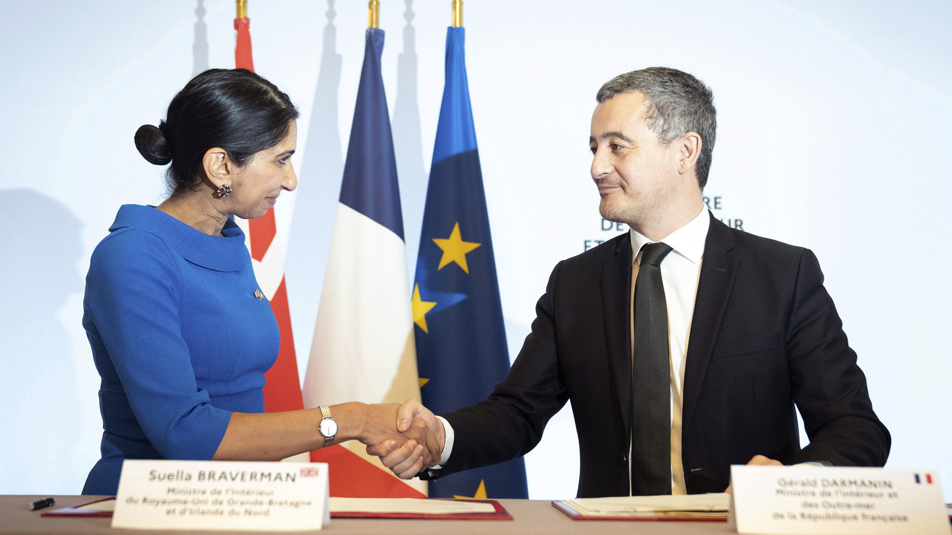 Die britische Innenministerin Suella Braverman und der französischen Innenminister Gerald Darmanin schütteln sich nach einer Vertragsunterzeichnung die Hand | AP