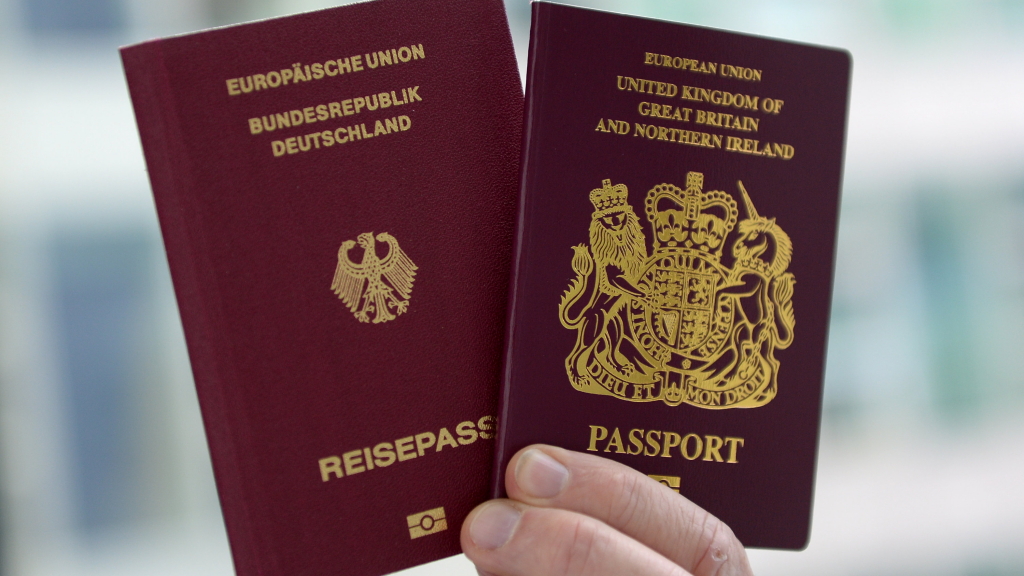 Eine Hand hält zwei Reisepässe: einen britischen und einen deutschen.