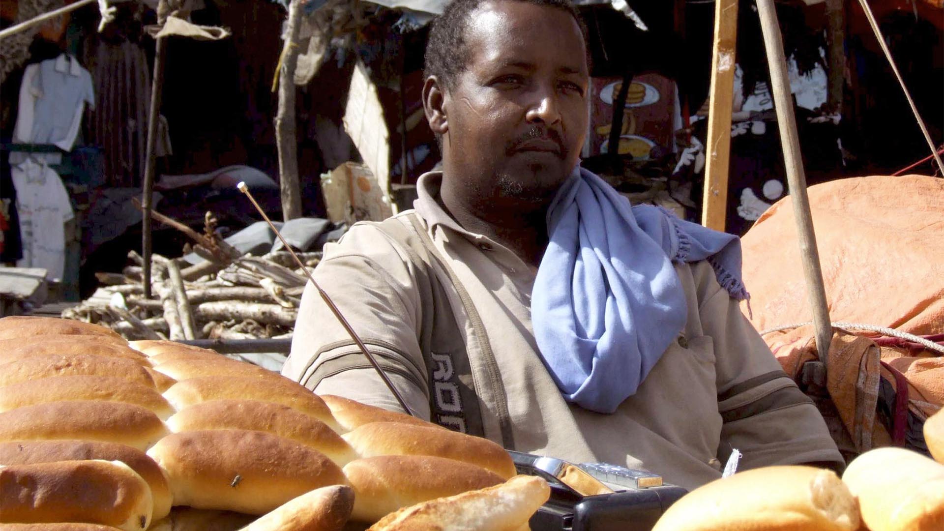 Ein Mann sitz an einem Marktstand und verkauft Brot.