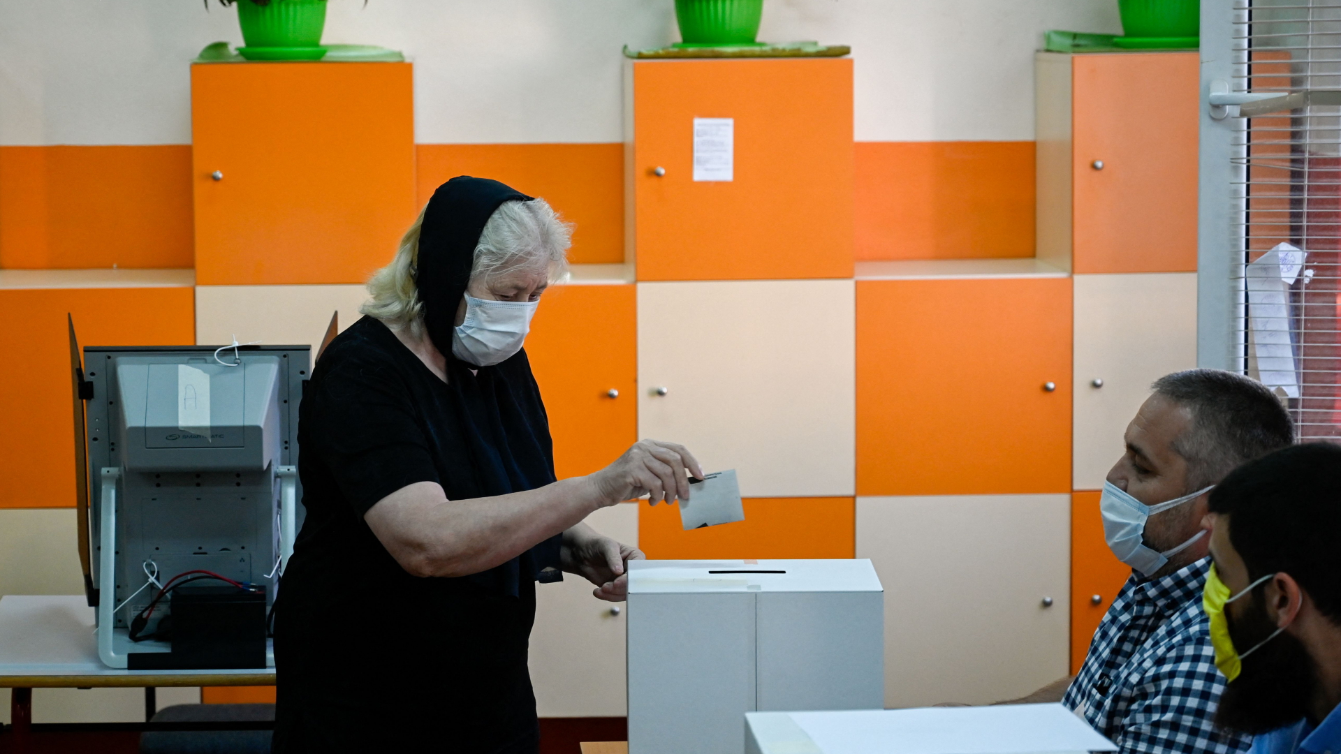 Eine ältere Frau mit Corona-Schutzmaske wirft in einem Wahllokal in Bulgarien ihren Stimmzettel in eine Urne.