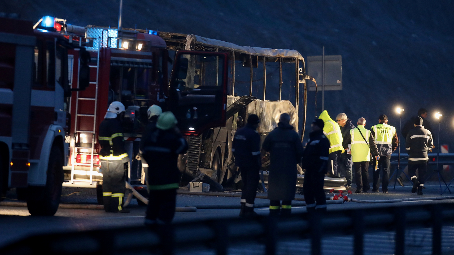 Rettungskräfte stehen an dem ausgebrannten Bus auf der Autobahn. | REUTERS
