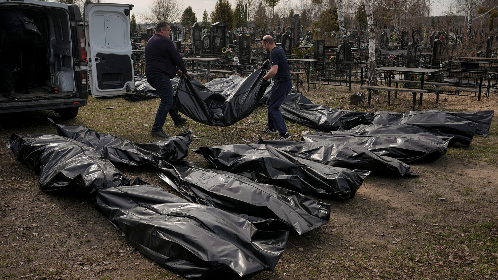 Arbeiter laden auf einem Friedhof in Butscha Leichen aus einem Transporter aus.