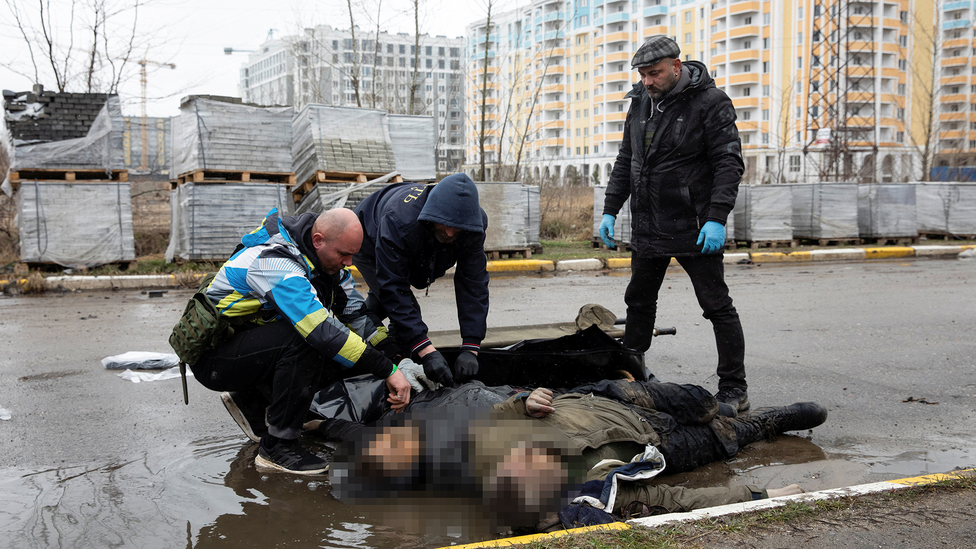 Männer kümmern sich um die Leichen von Menschen, die in Butscha auf einer Straße liegen.