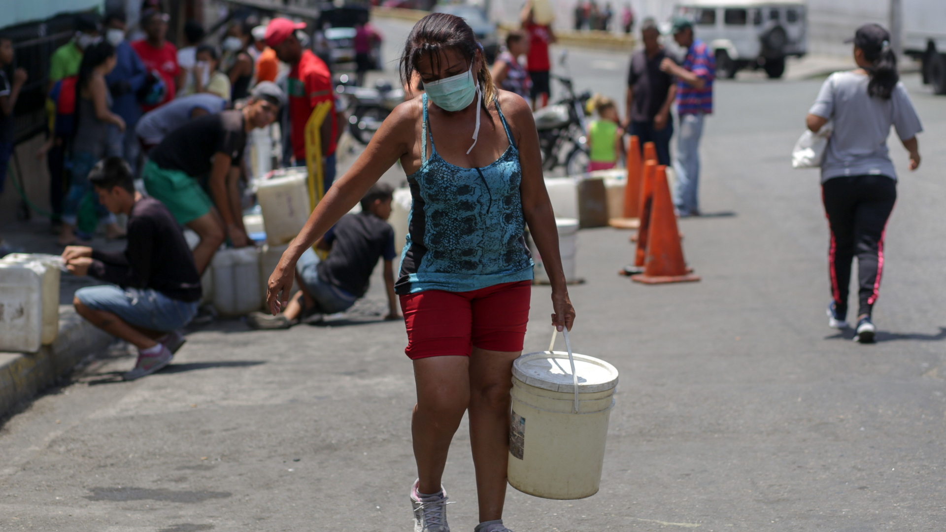Eine Frau mit Schutzmaske trägt in Caracas einen Eimer mit Wasser über die Straße, den sie sich zuvor abgefüllt hat | AFP