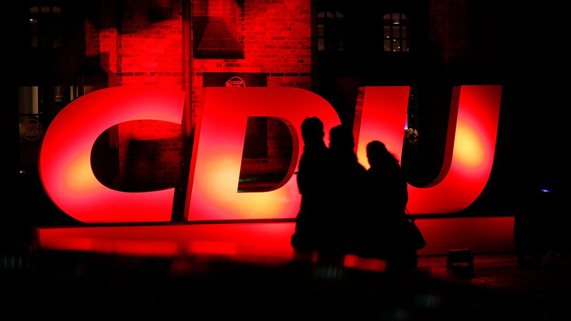 Menschen laufen vor einem beleuchteten CDU-Logo vorbei | AFP