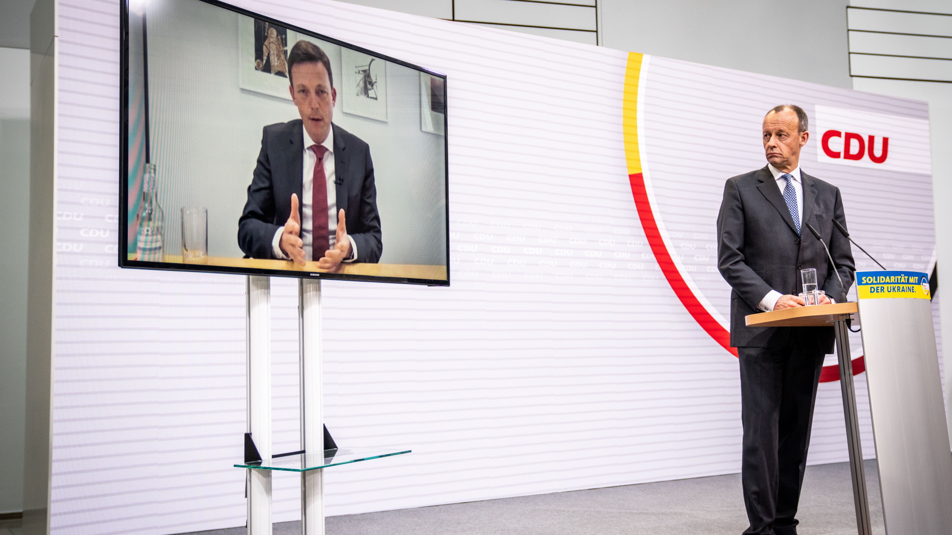 Der CDU-Bundesvorsitzende Friedrich Merz blickt bei einer Pressekonferenz nach der Wahl im Saarland im März 2022 zu einem Fernseher, auf dem der abgewählte Ministerpräsident Tobias Hans zu sehen ist. | dpa