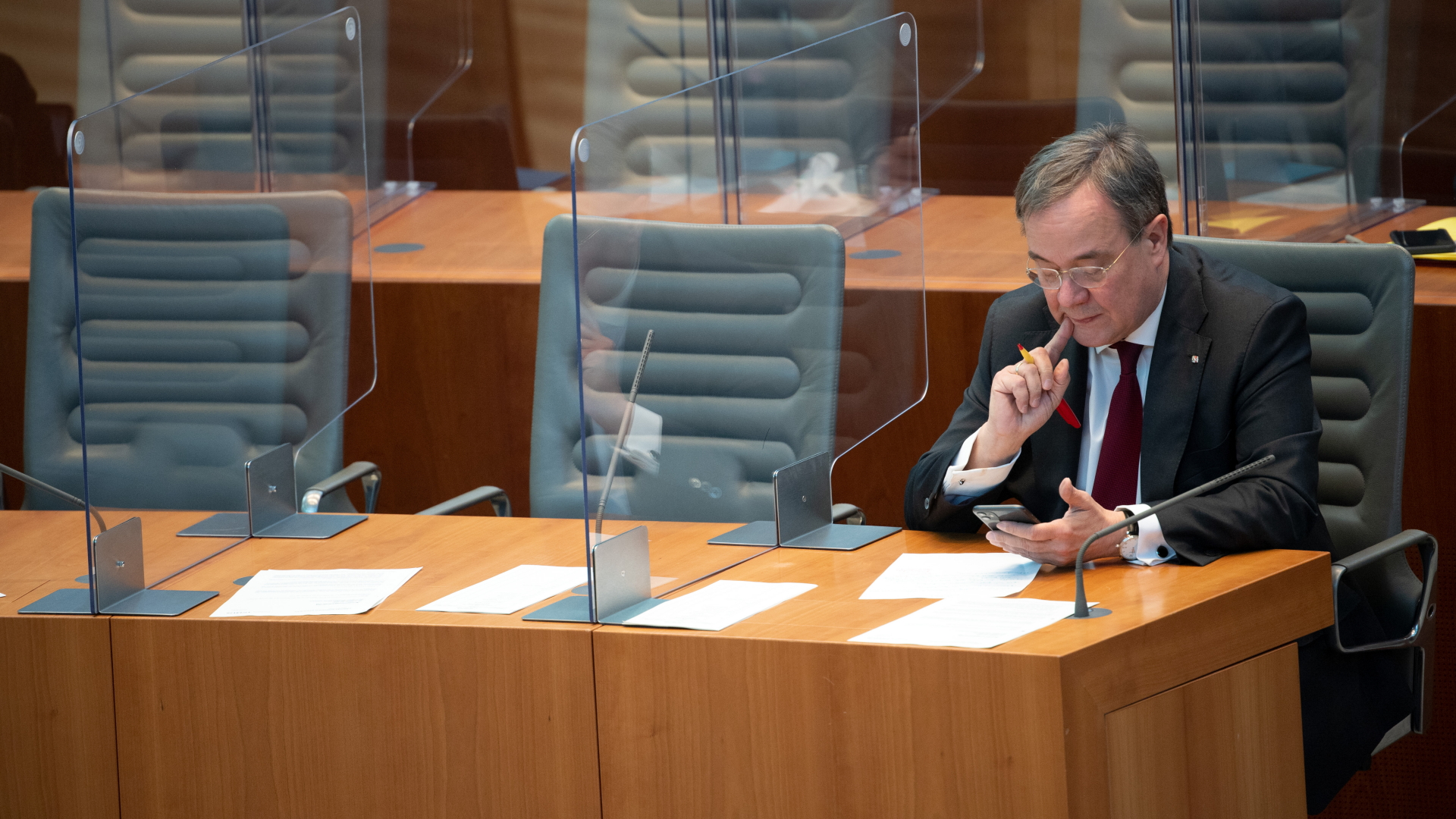 Nordrhein-Westfalens Ministerpräsident Laschet blickt im leeren Landtag auf sein handy. | dpa