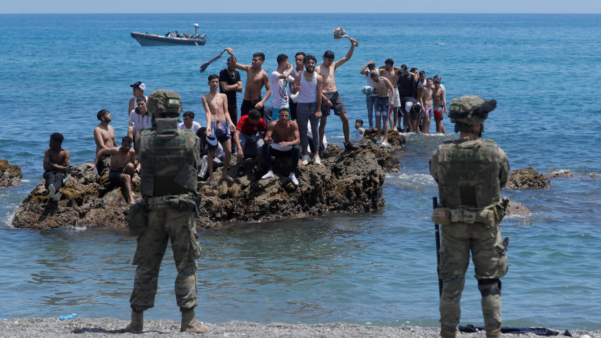 Migranten stehen auf einem Fels im Wasser in Ceuta und werden von Soldaten bewacht | REUTERS