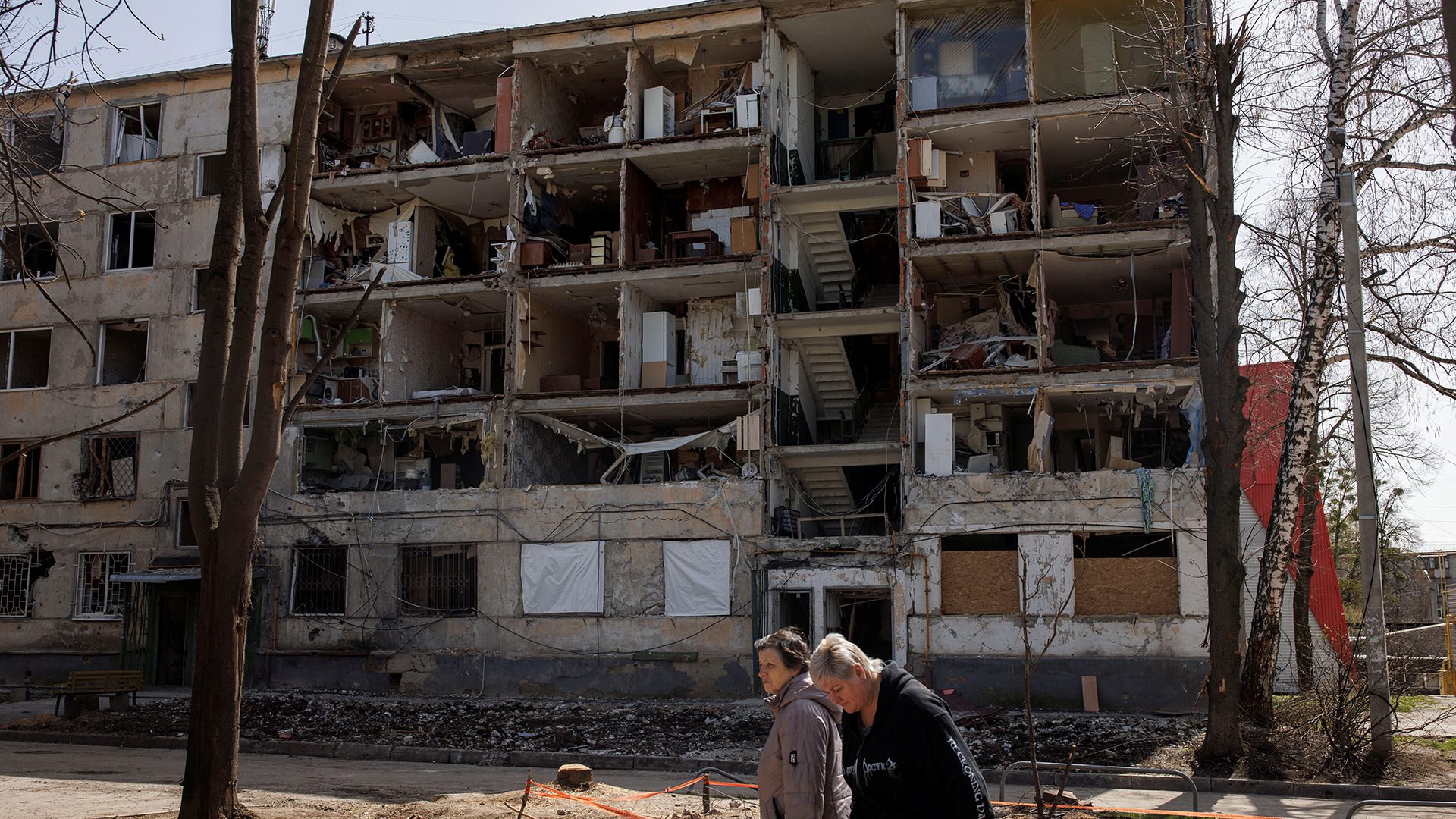Zwei Menschen vor einem zerstörten Wohnblock in Charkiw, Ukraine. | REUTERS