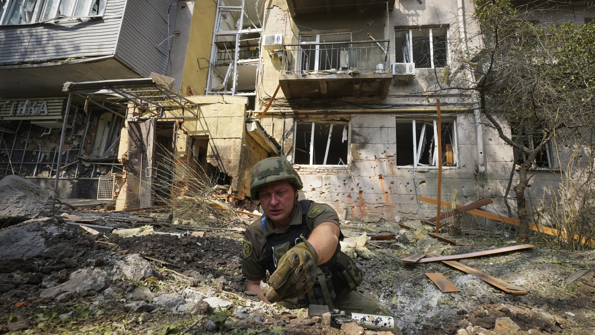 Ein ukrainischer Soldat liegt in einem Explosionskrater vor einem stark beschädigten Wohnhaus im ostukrainischen Charkiw. | AP