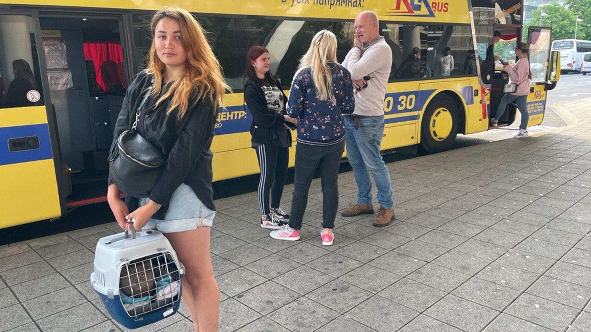 Eine Frau steht mit einer Katzenbox vor einem gelben Reisebus. | Report Mainz / SWR