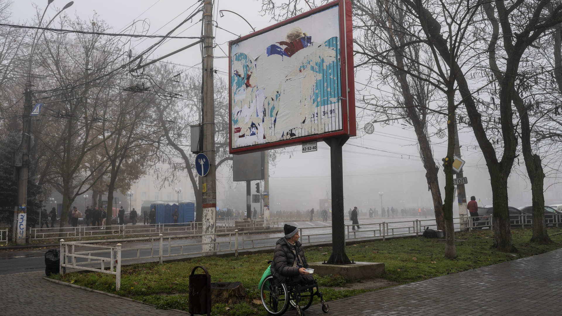 Ein Rollstuhlfahrer bettelt unter einer Plakatwand in der südukrainsichen Stadt Cherson. | AP