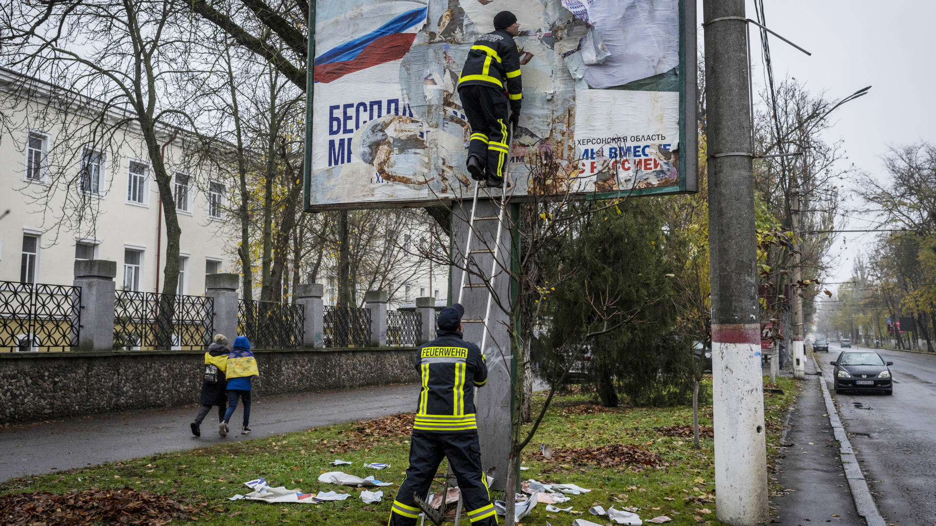 Feuerwehrleute entfernen ein russisches Plakat in Cherson. | dpa