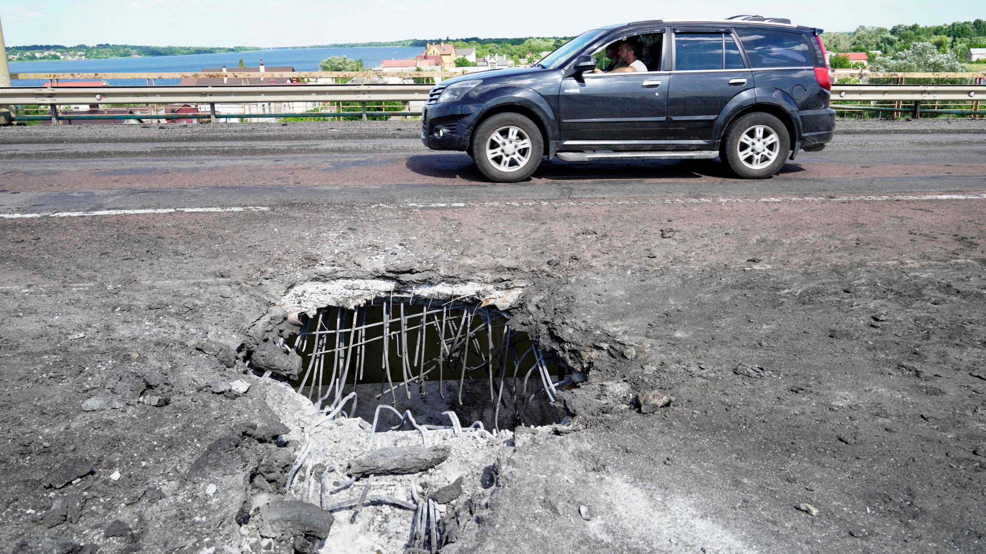 Ein Auto hält vor einem Krater, den ein Geschoss in die Antoniwskyj-Brücke bei Cherson geschlagen hat. | AFP