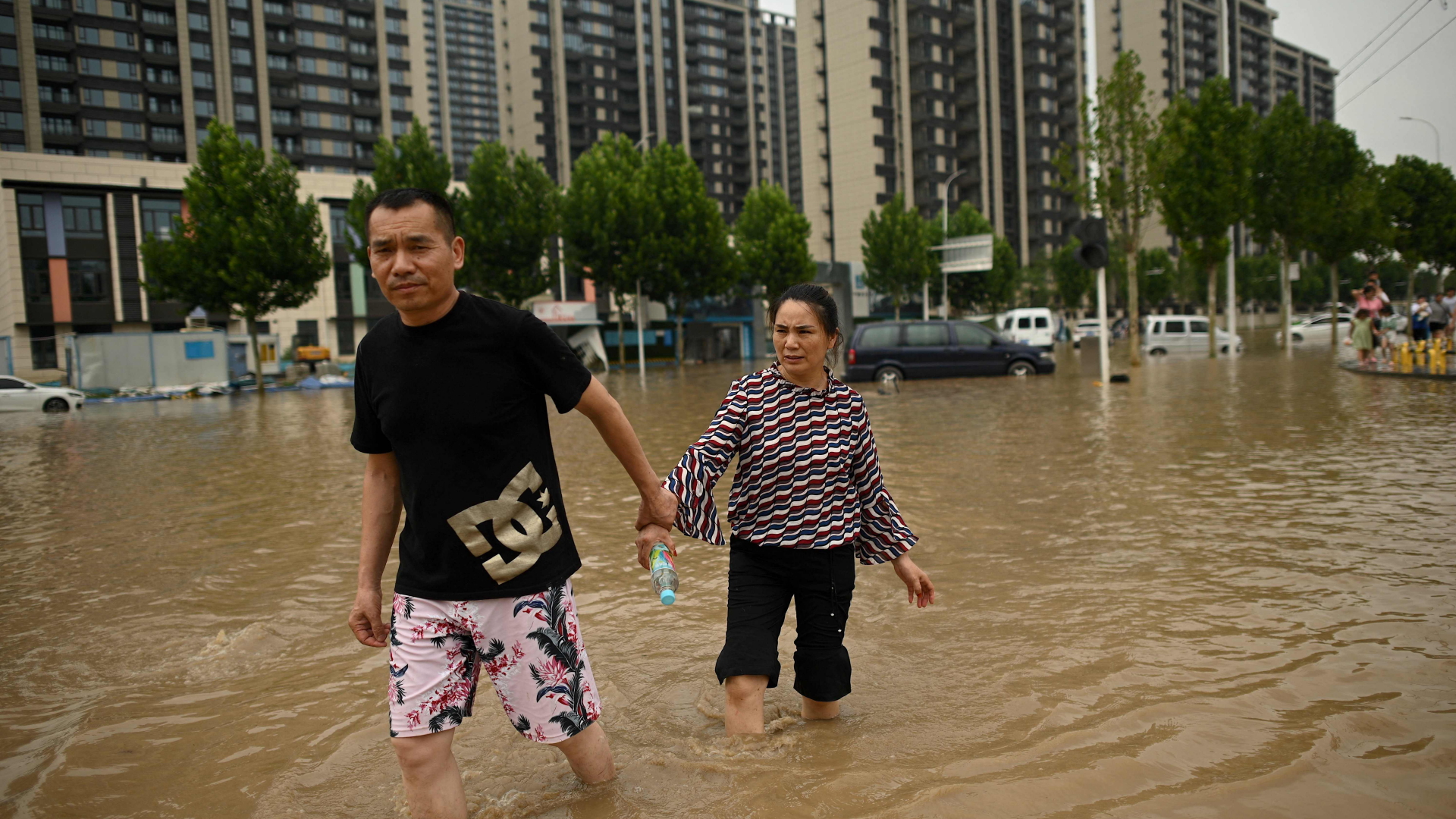 Zwei Menschen waten in einer überfluteten Straße durch das Wasser.  | AFP