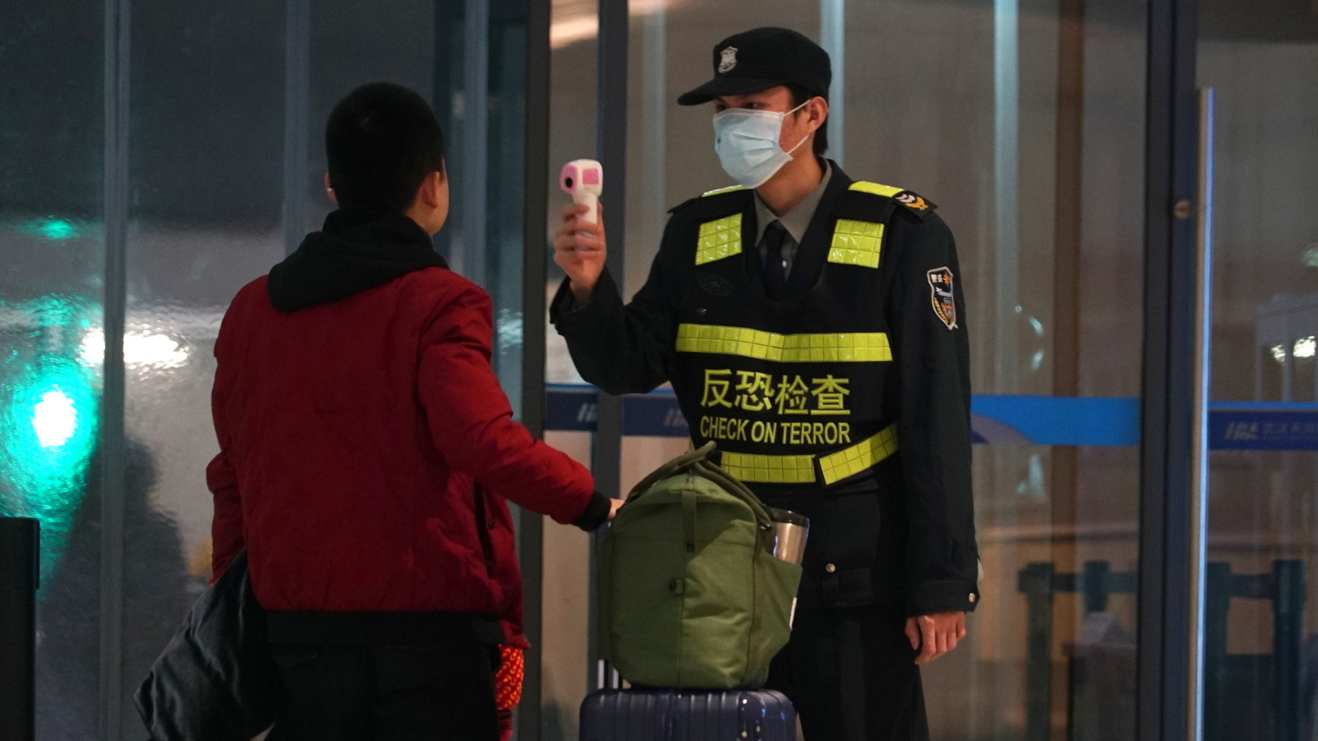 Ein Mitarbeiter des Flughafen Wuhan Tianhe International Airport trägt Mundschutz und misst bei einem Reisenden Temperatur. | 