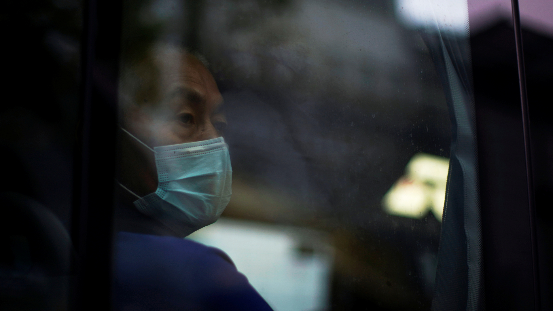 Ein Mann mit einer Atemschutzmaske sitzt in einem Bus in Shanghai (Archivbild). | REUTERS