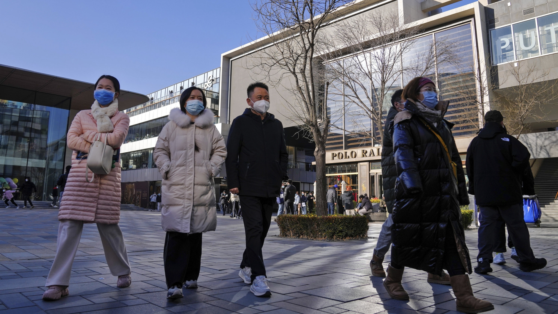 Passanten laufen mit Schutzmasken an einem nach dem Corona-Lockdown neu eröffneten Einkaufszentrum in Peking vorbei. | AP
