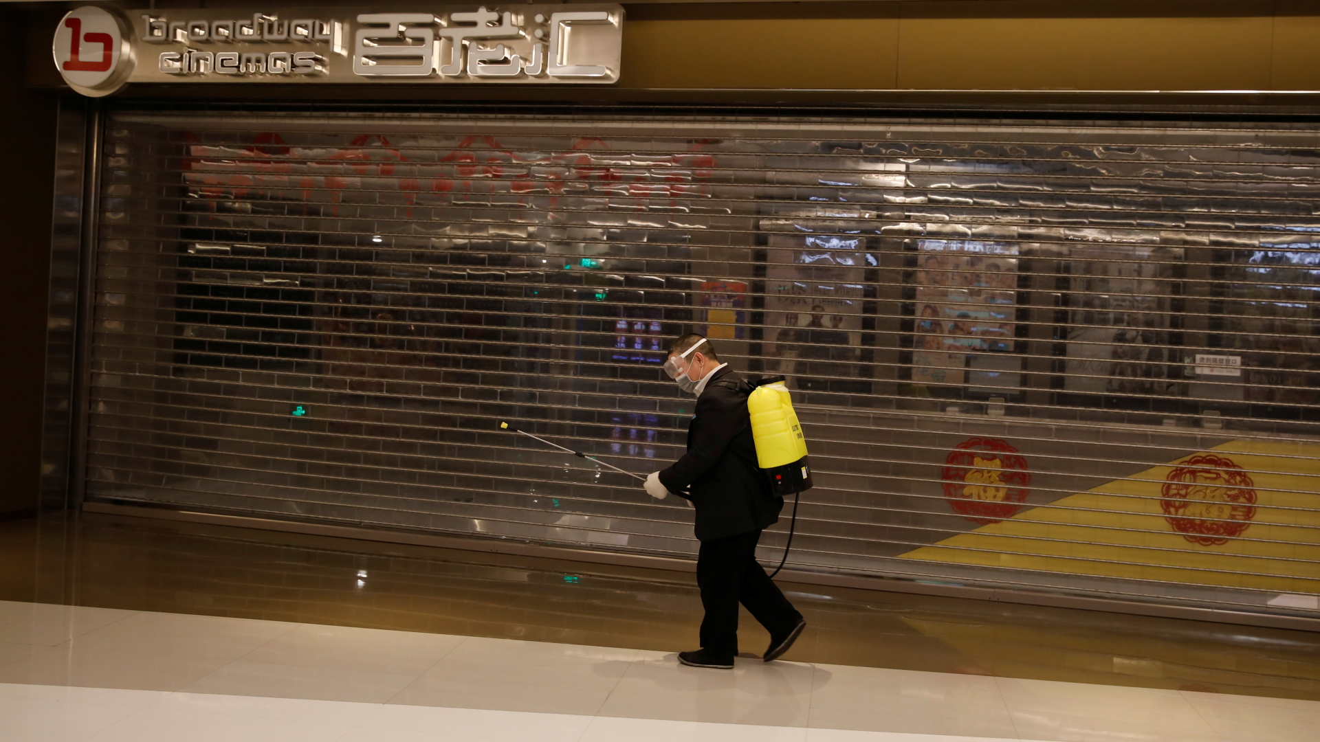 Ein Mann läuft mit einem Desinfektions-Sprühgerät an einem geschlossenen Kino in einem Pekinger Einkaufszentrum vorbei. | REUTERS