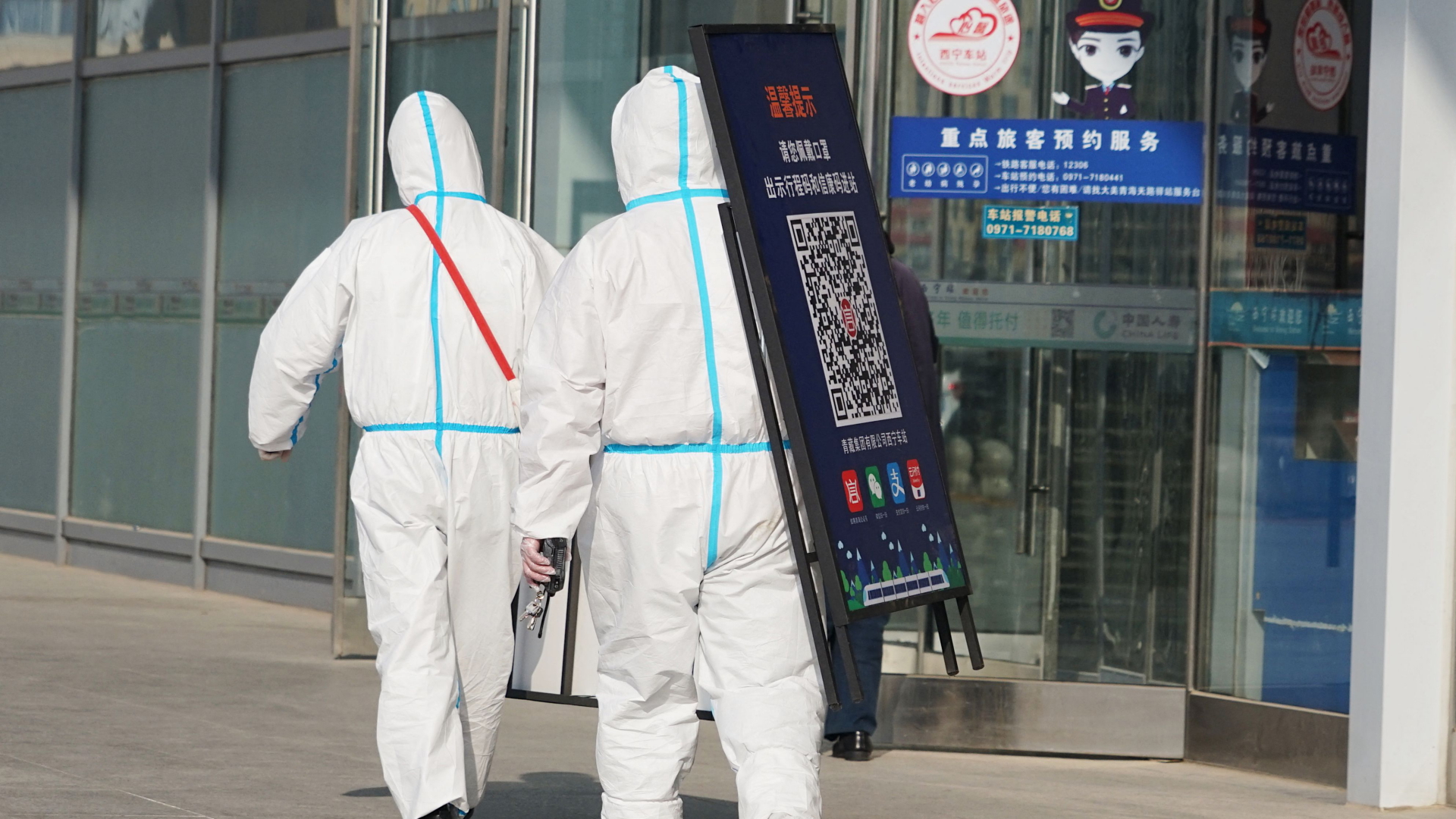 Mitarbeiter entfernen ein Plakat mit einem Code, der beim Betreten des Bahnhofs von Xining in China wegen der Corona-Pandemie genutzt werden musste. | AFP