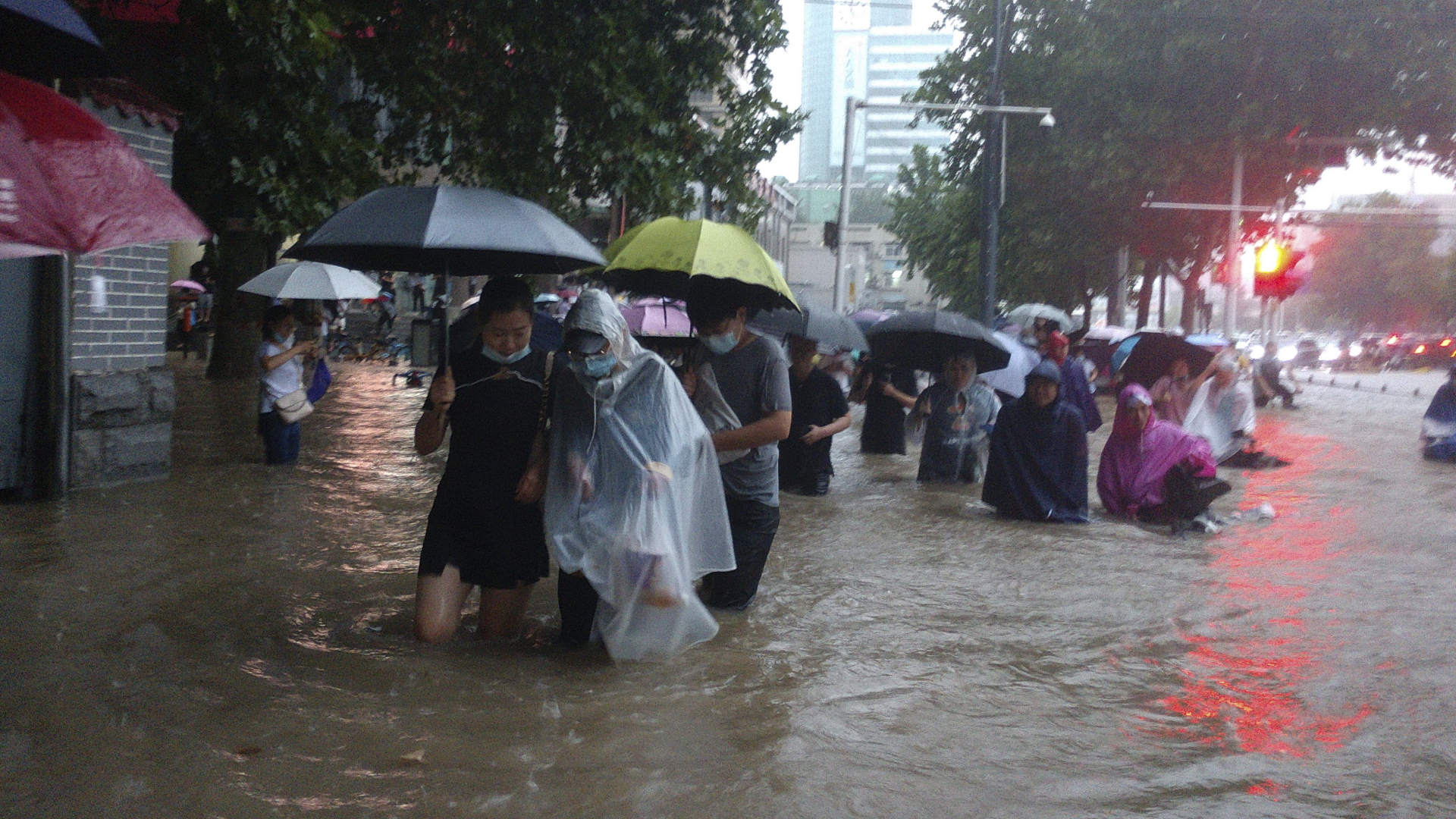 Menschen waten in der zentralchinesischen Provinz Henan durch eine überflutete Straße. | dpa