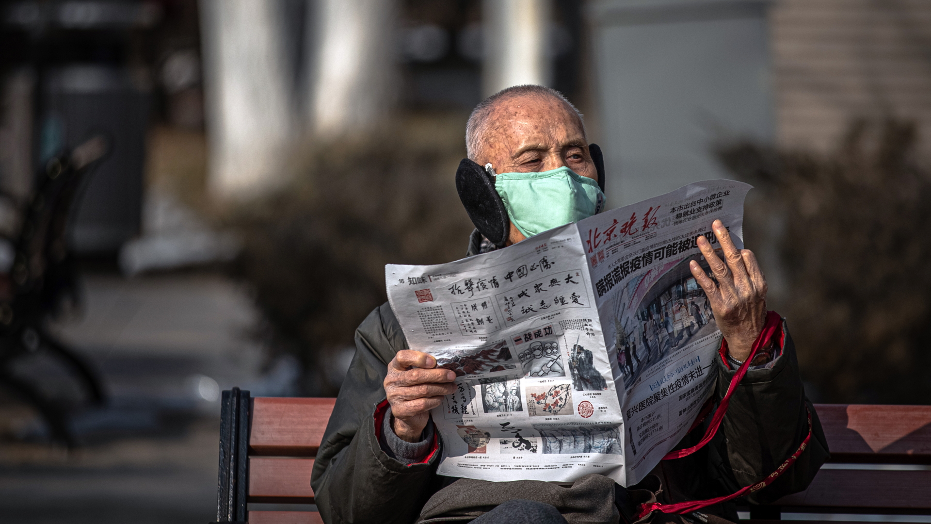 Ein älterer Mann mit Mundschutz sitzt in Peking auf einer Bank und liest Zeitung. | ROMAN PILIPEY/EPA-EFE/REX