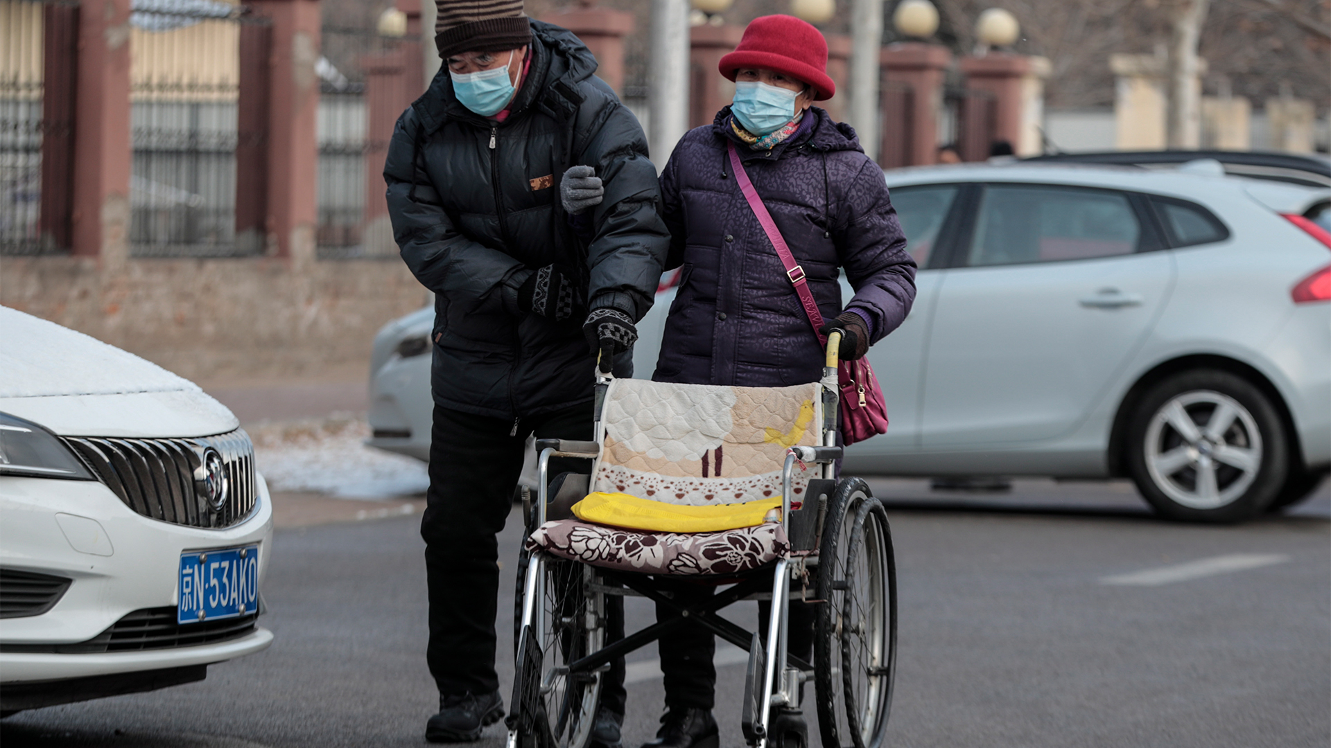 Zwei ältere Menschen gehen in Peking eine Straße entlang und schieben einen Rollstuhl. | EPA