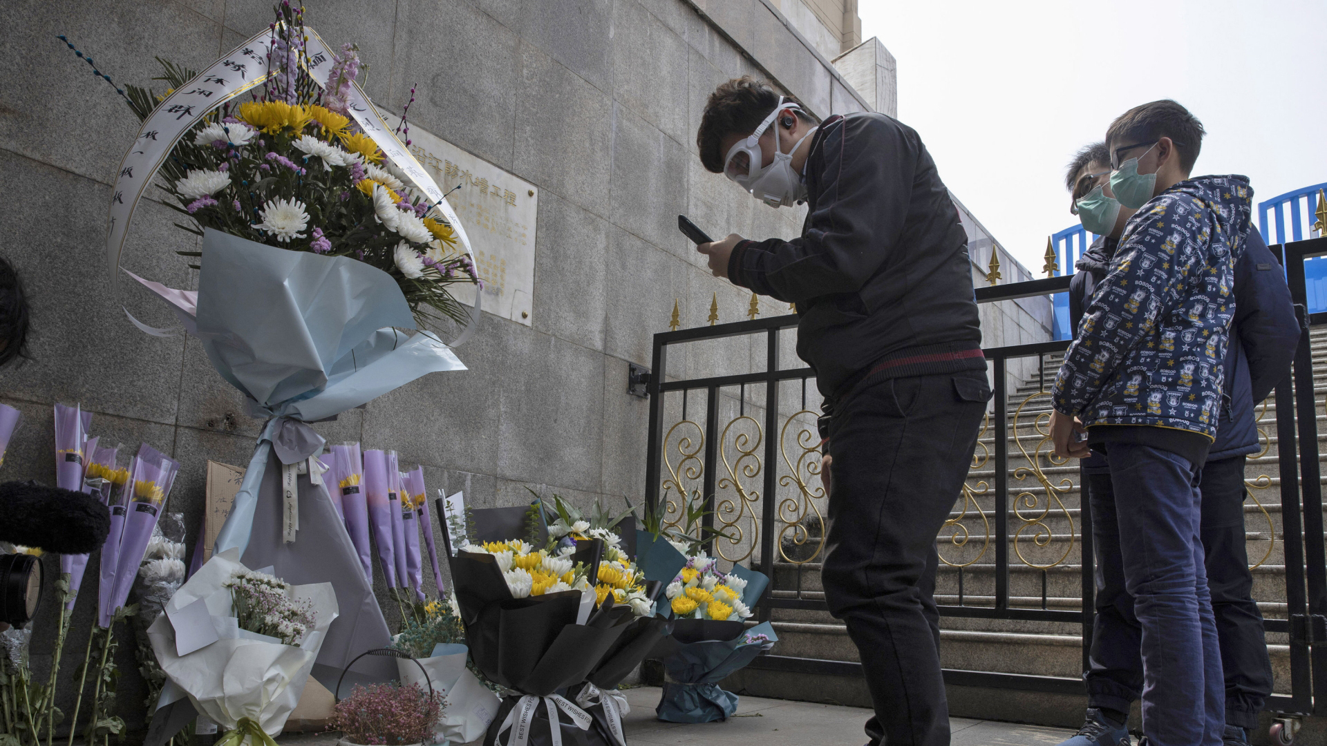 Trauernde in Schutzmasken verbeugen sich vor einem Heldenmonument in Wuhan, an dem sie Blumen niedergelegt haben. | AP