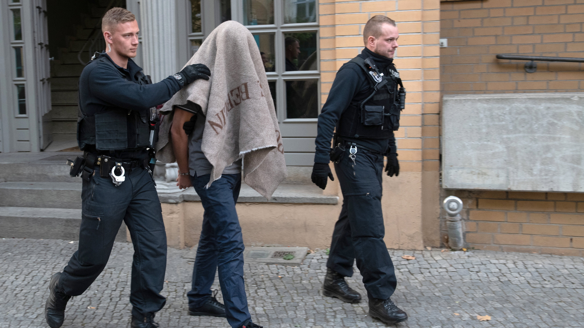Polizisten führen verdächtigen Mann nach Razzia in Berlin-Tiergarten ab.  | dpa