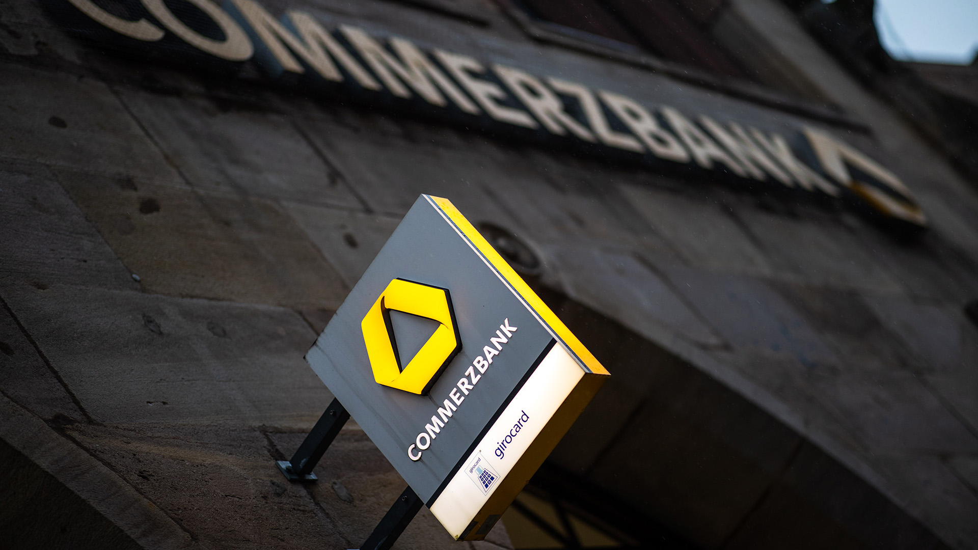Ein beleuchtetes Schild der Commerz-Bank vor einer dunklen Hauswand | dpa