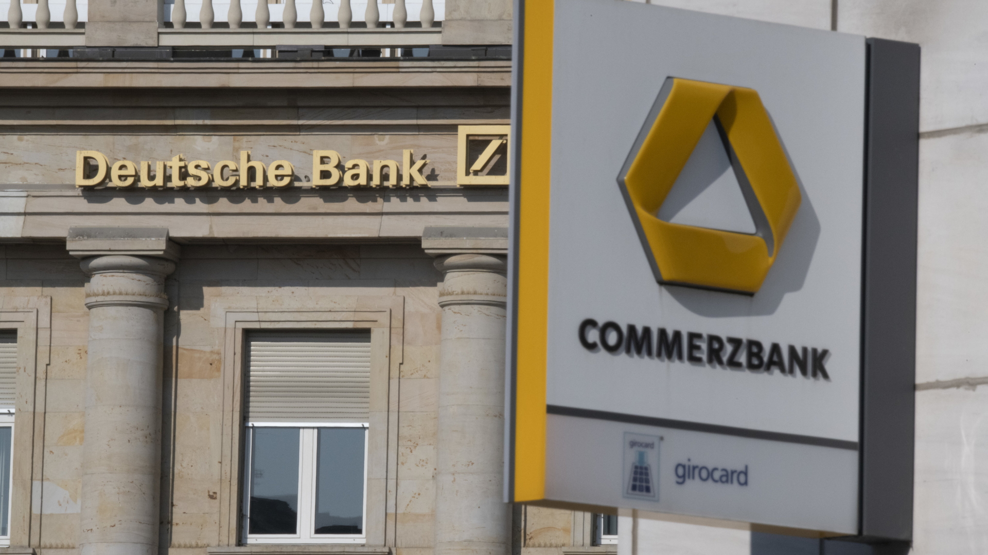 Der Schriftzug Deutsche Bank neben dem Logo iost auf einer Hauswand zu lesen, im Vordergrund ein Schild mit der Commerzbank mit Logo.