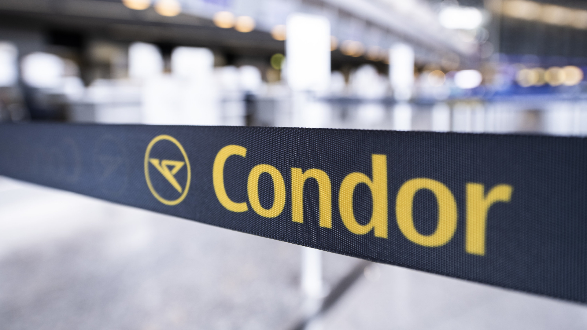 Das Logo der Fluggesellschaft Condor ist auf dem Absperrband in einer Abflughalle zu sehen | dpa