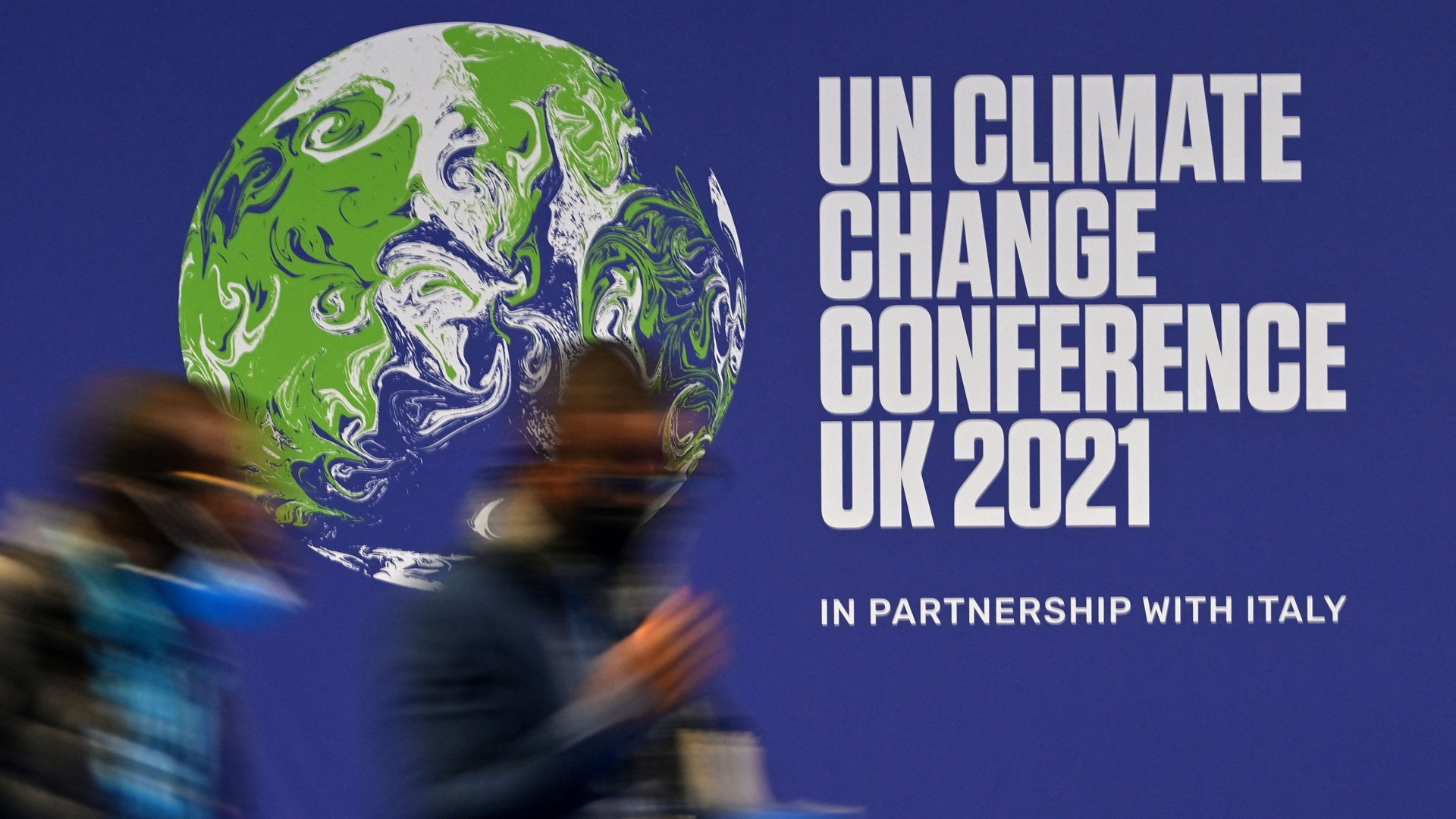 Zwei Menschen laufen an einem Plakat der UN-Klimakonferenz in Glasgow vorbei. | AFP