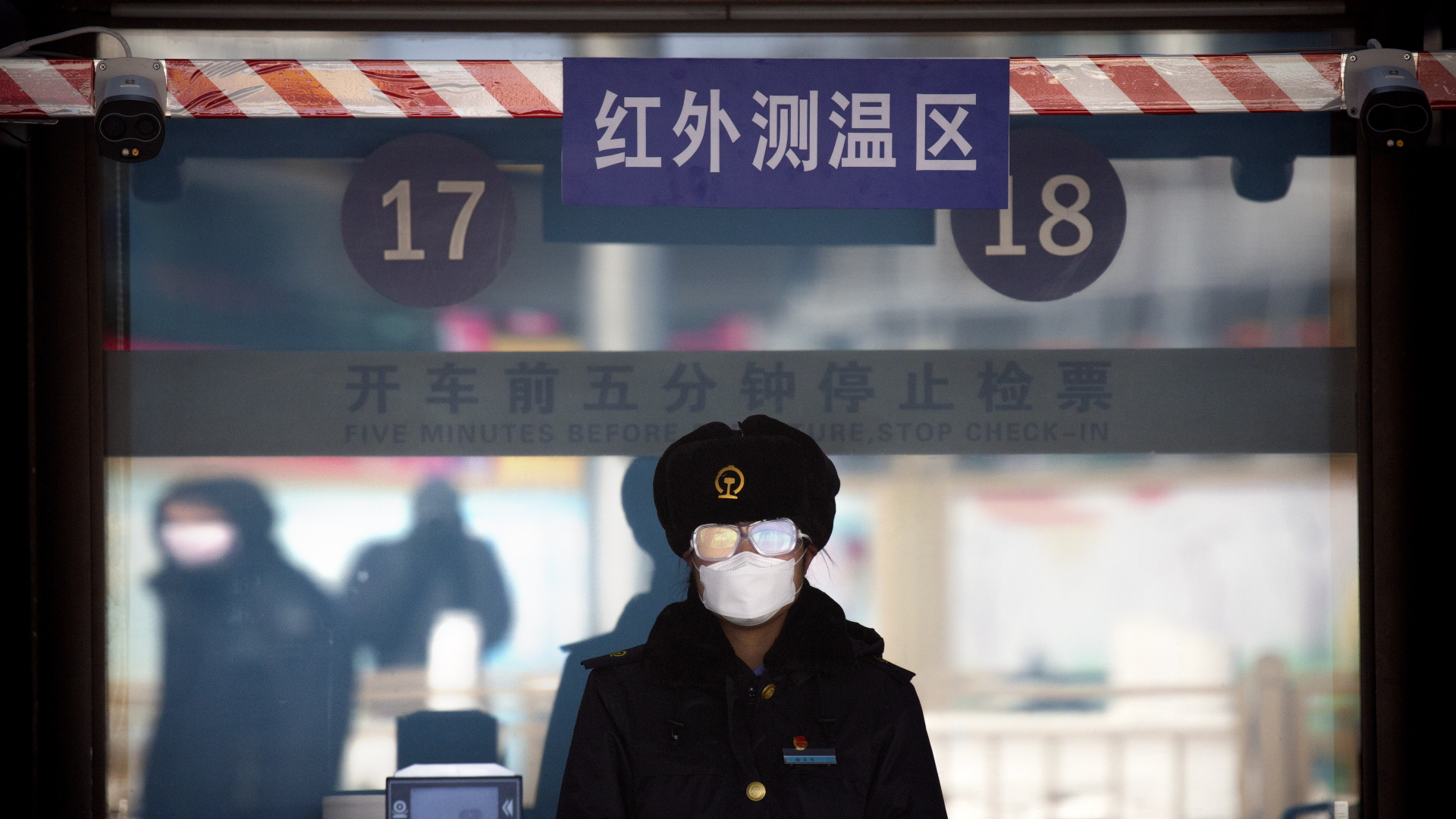 Eine Bahnhofsangestellte trägt einen Mundschutz und eine Schutzbrille, während sie darauf wartet, die Fahrkarten der Passagiere am Bahnhof von Peking zu kontrollieren. 
